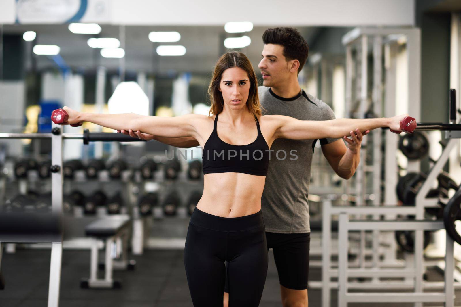 Personal trainer helping a young woman lift dumbells while working out in a gym