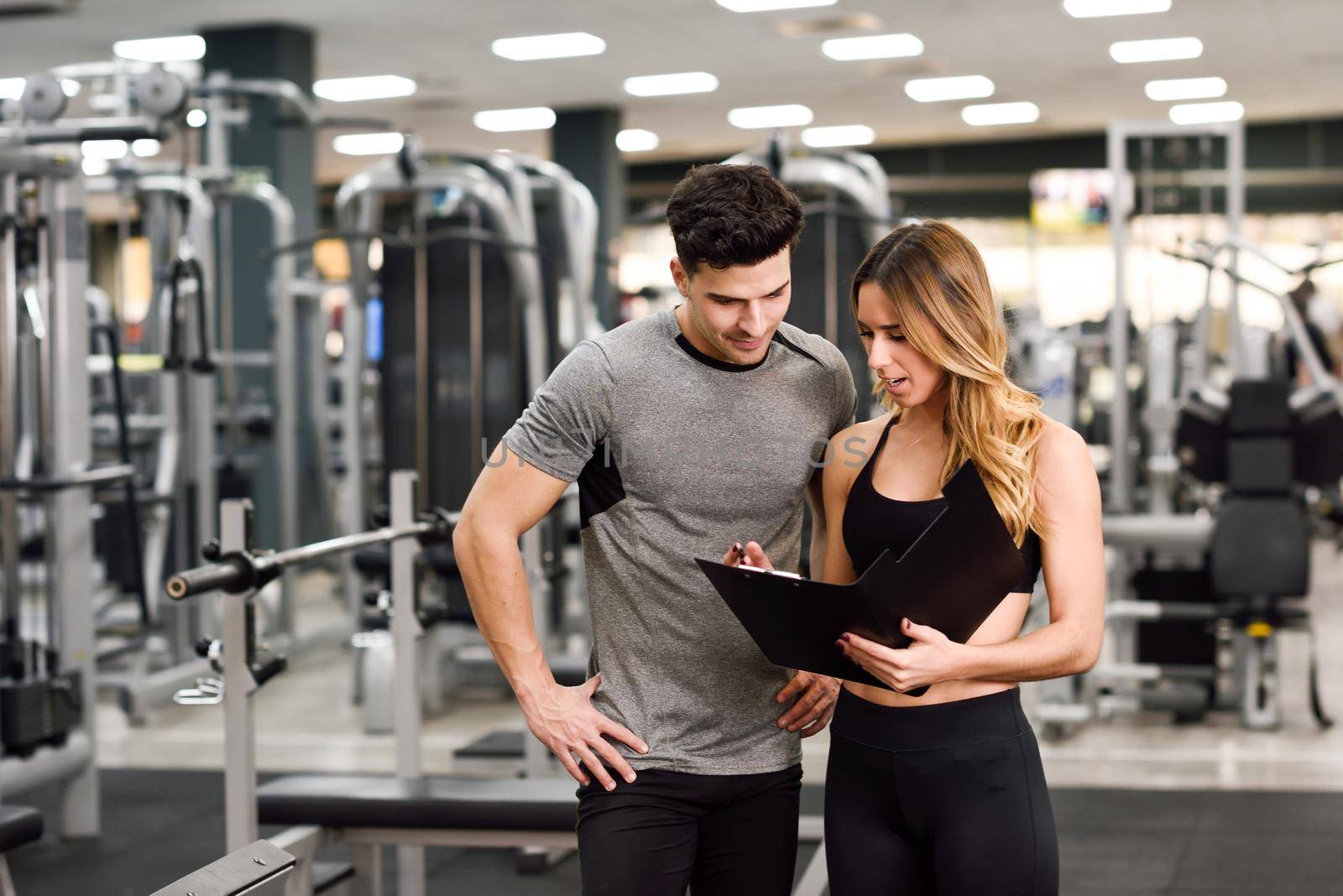 Personal trainer and client looking at his progress at the gym. Athletic man and woman wearing sportswear.