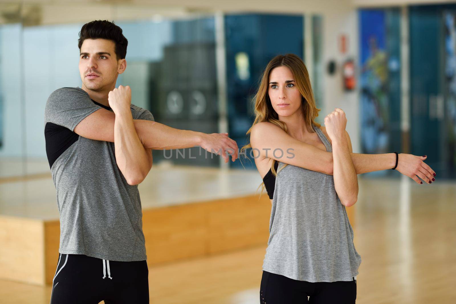 Young woman and man working out indoors. Two people stretching their arms in a gym.