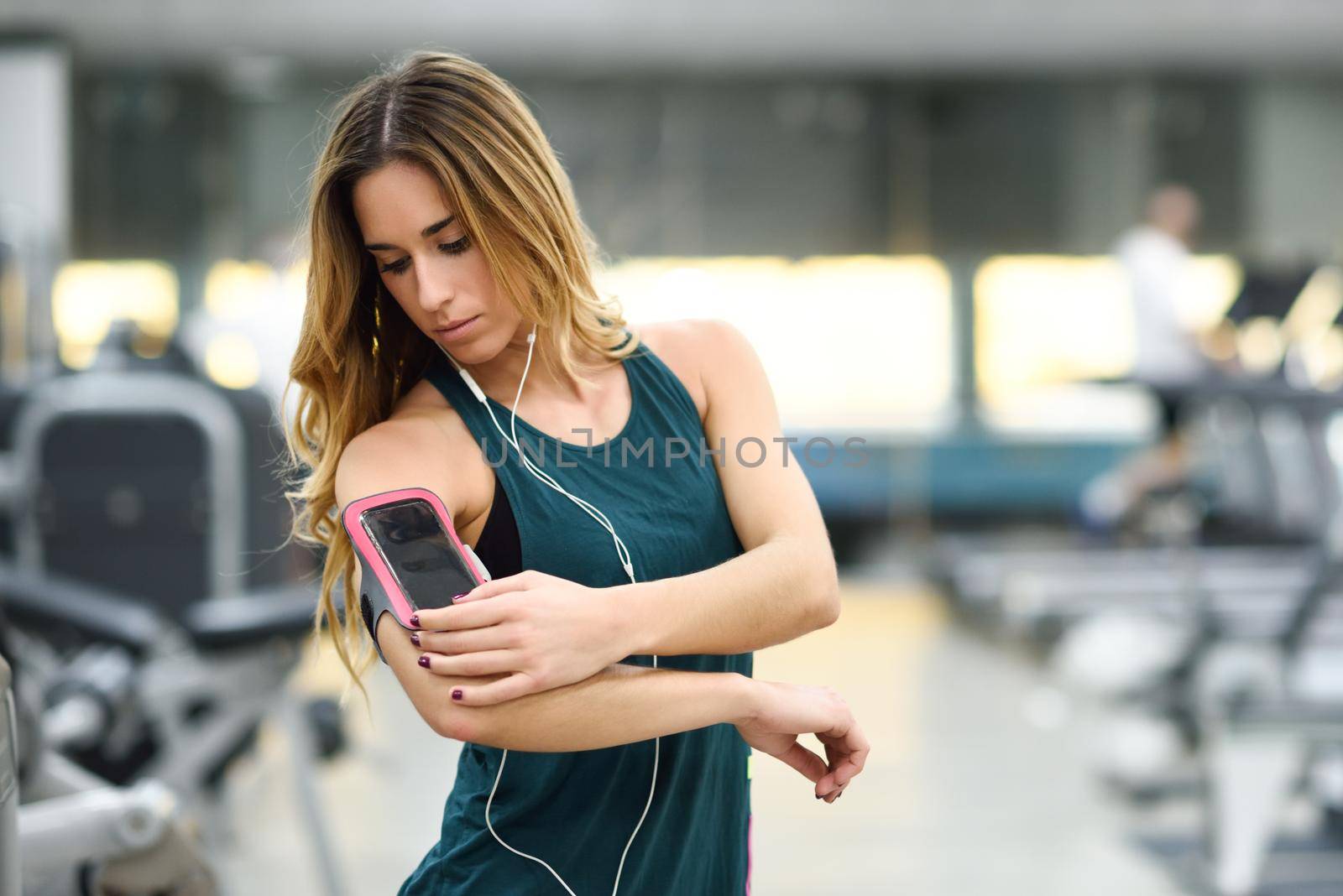 Young woman using smartphone standing in the gym by javiindy