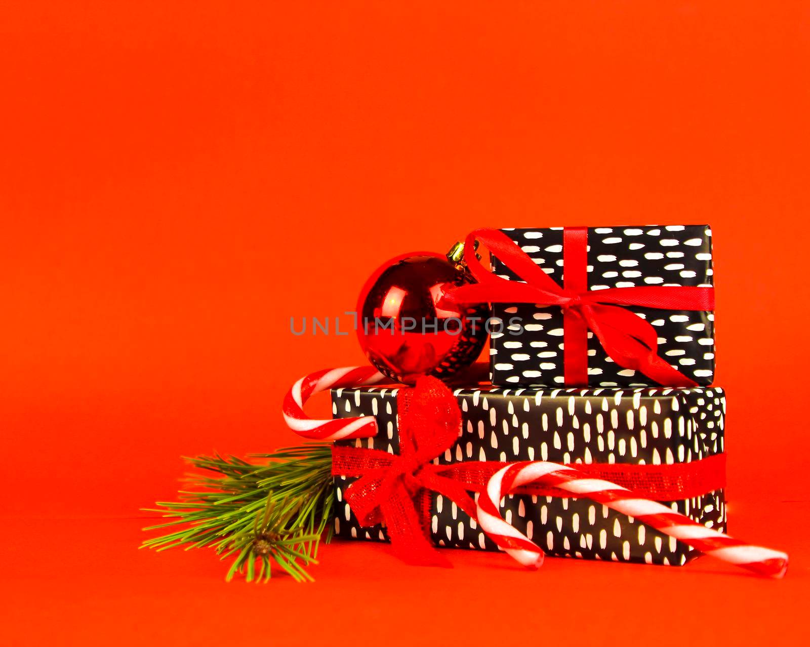 Gifts wrapped with black and white paper and red bows next to Christmas decoration on red background