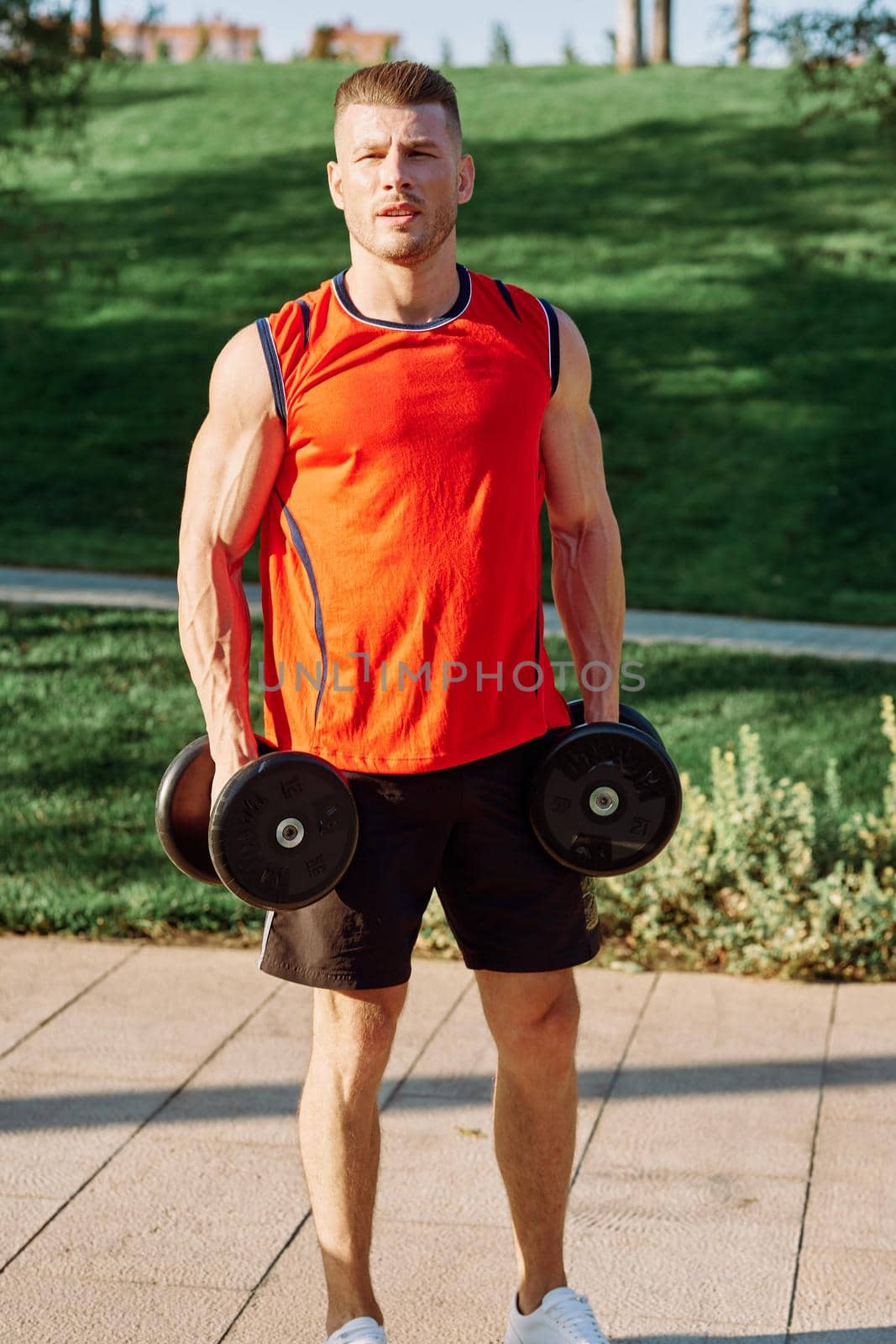athletic man with dumbbells in his hands outdoors in the park by Vichizh