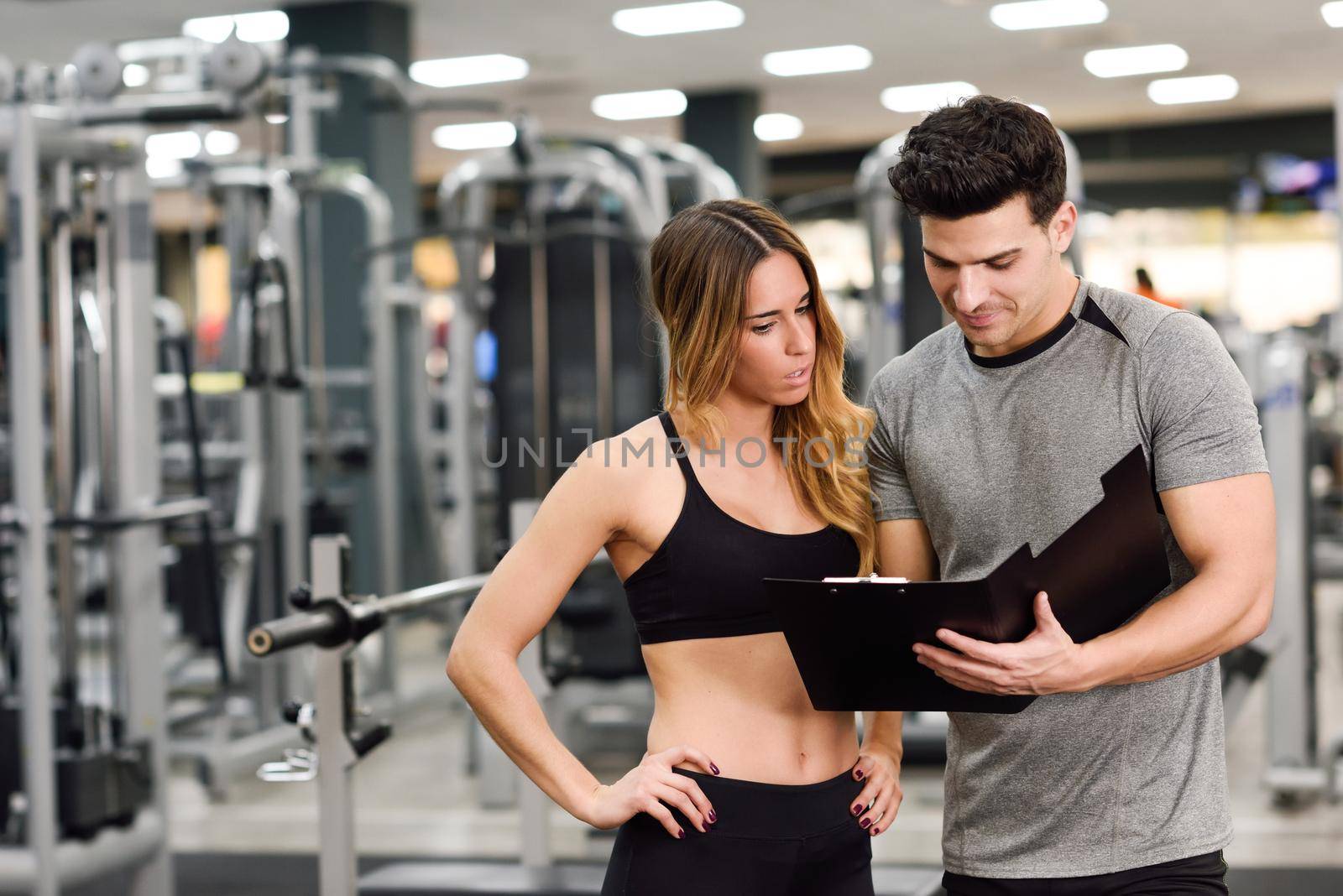 Personal trainer and client looking at her progress at the gym by javiindy