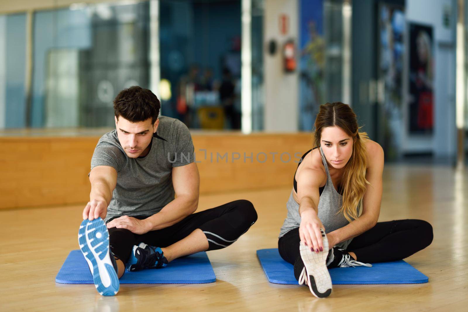Two people streching their legs in gym. by javiindy