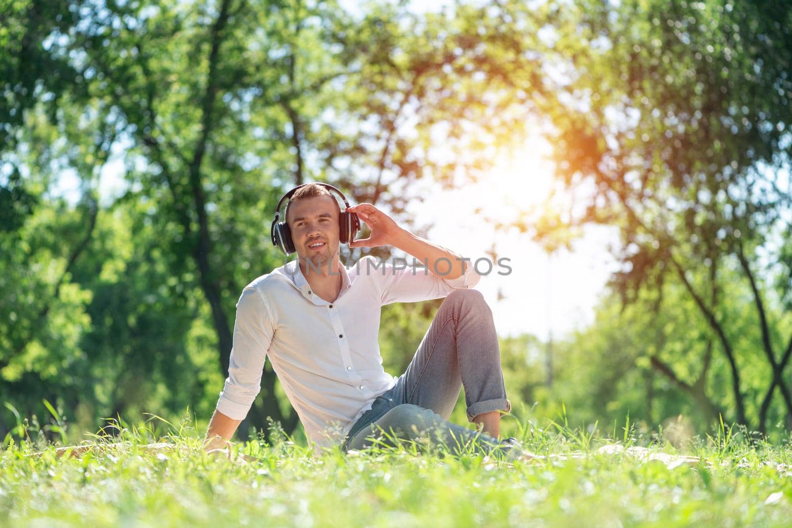 Young man in the park listens to music. He sits on the grass and enjoys music.