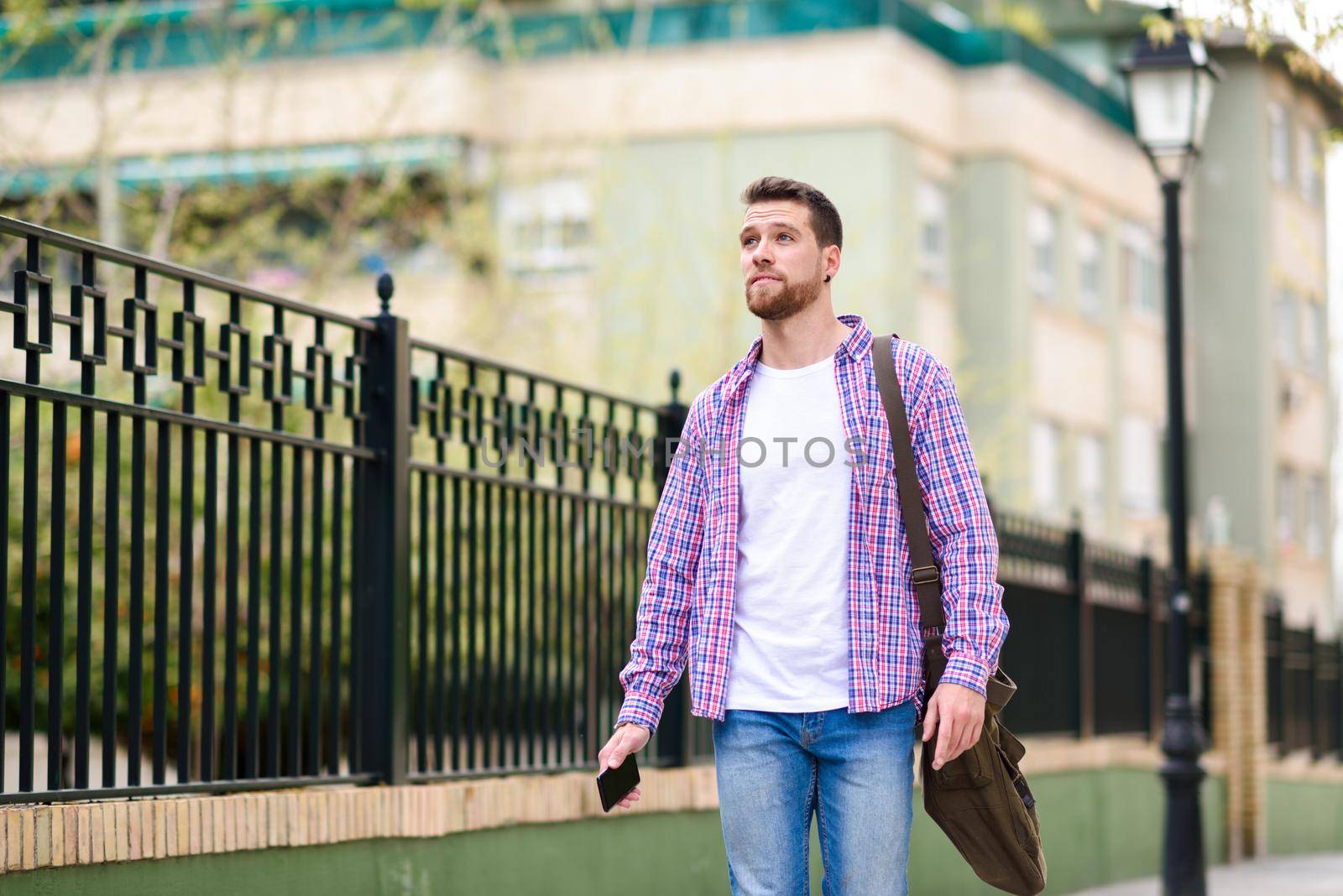 Young bearded man walking in urban background. Traveler wearing casual clothes. Lifestyle concept.