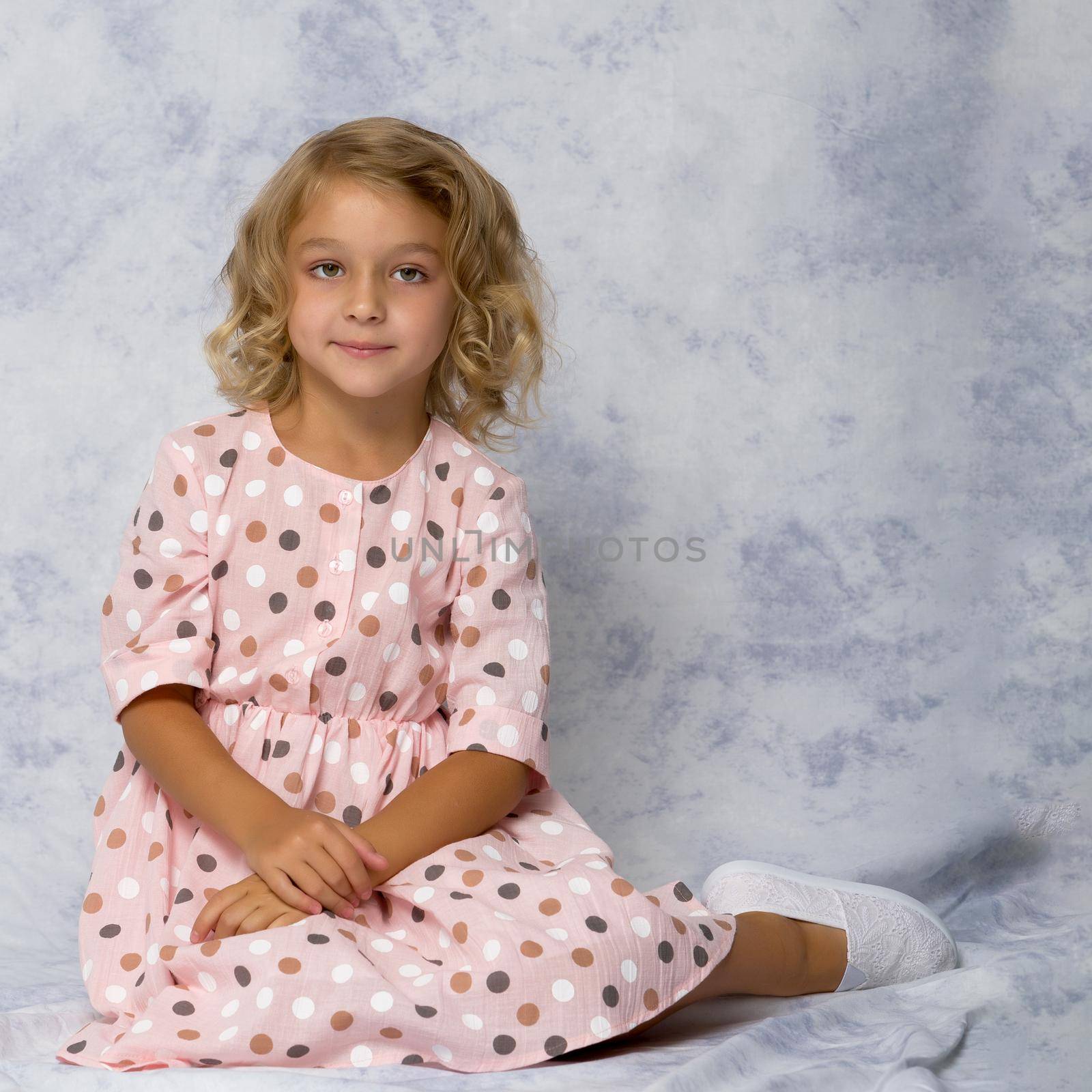 Beautiful little girl is sitting on the floor in the studio. The concept of a happy childhood, beauty and fashion.