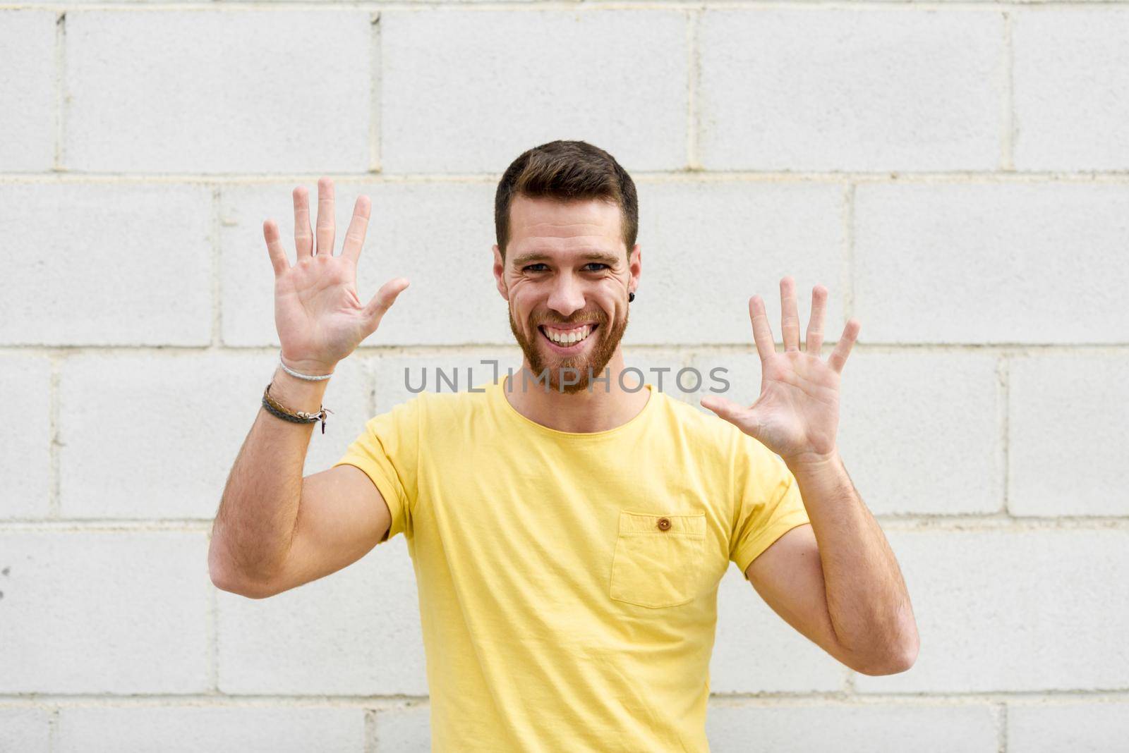 Funny young man on brick wall with open hands smiling. Guy wearing casual clothes in urban background.