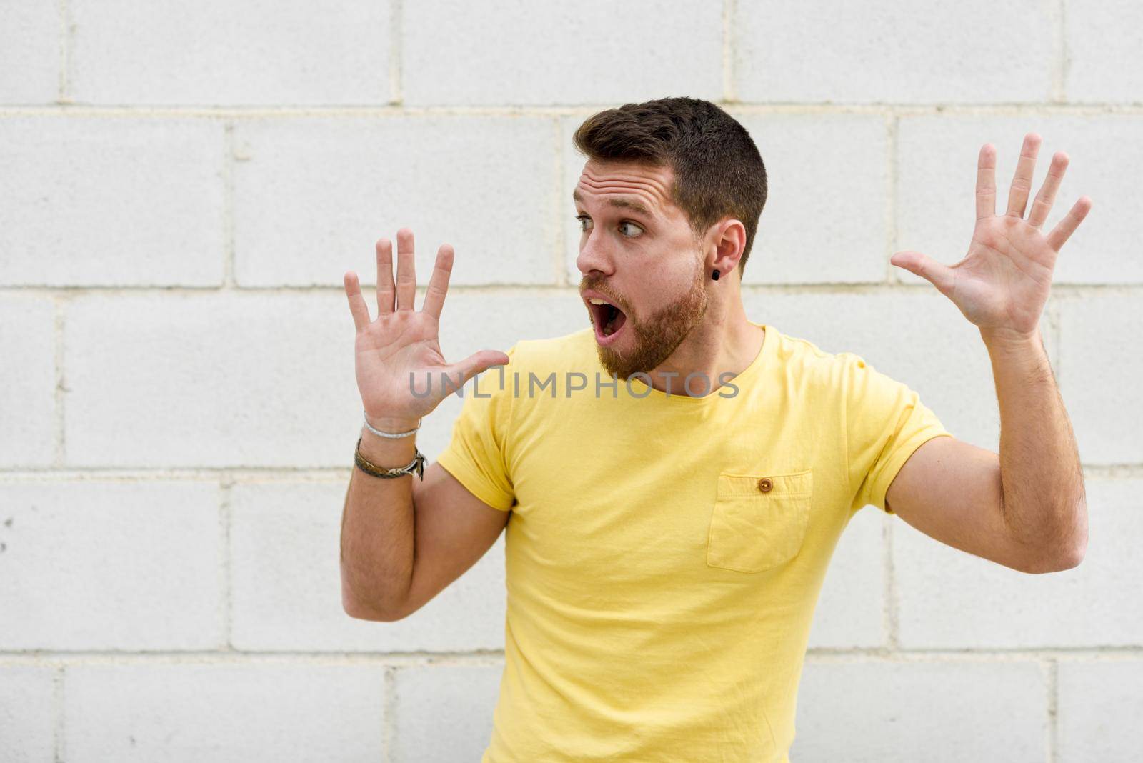 Funny young man on brick wall with open hands looking at leftside. Guy wearing casual clothes in urban background.