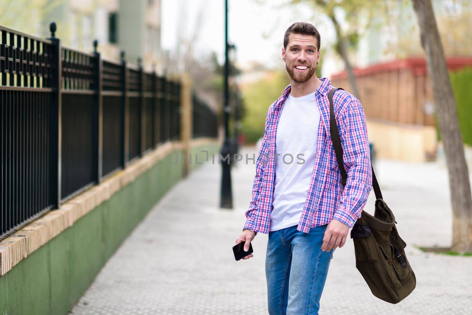 Young bearded man smiling in urban background. Traveler wearing casual clothes. Lifestyle concept.