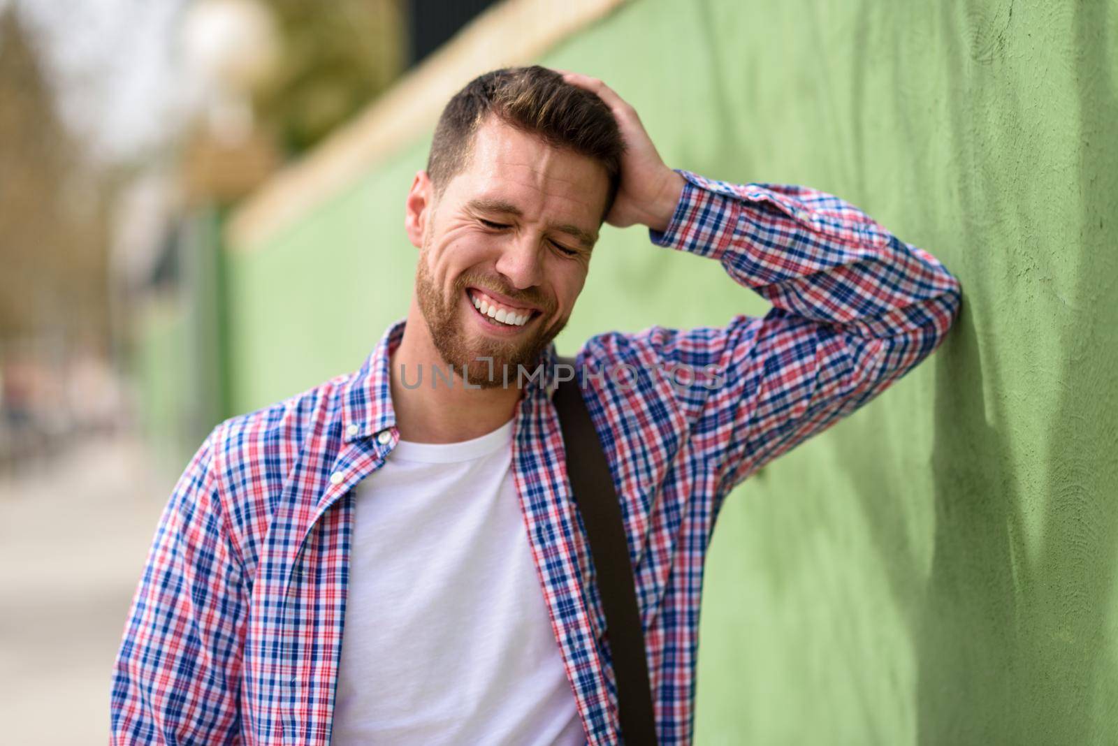 Attractive young man laughing outdoors. Funny guy wearing casual clothes in urban background. Lifestyle concept.