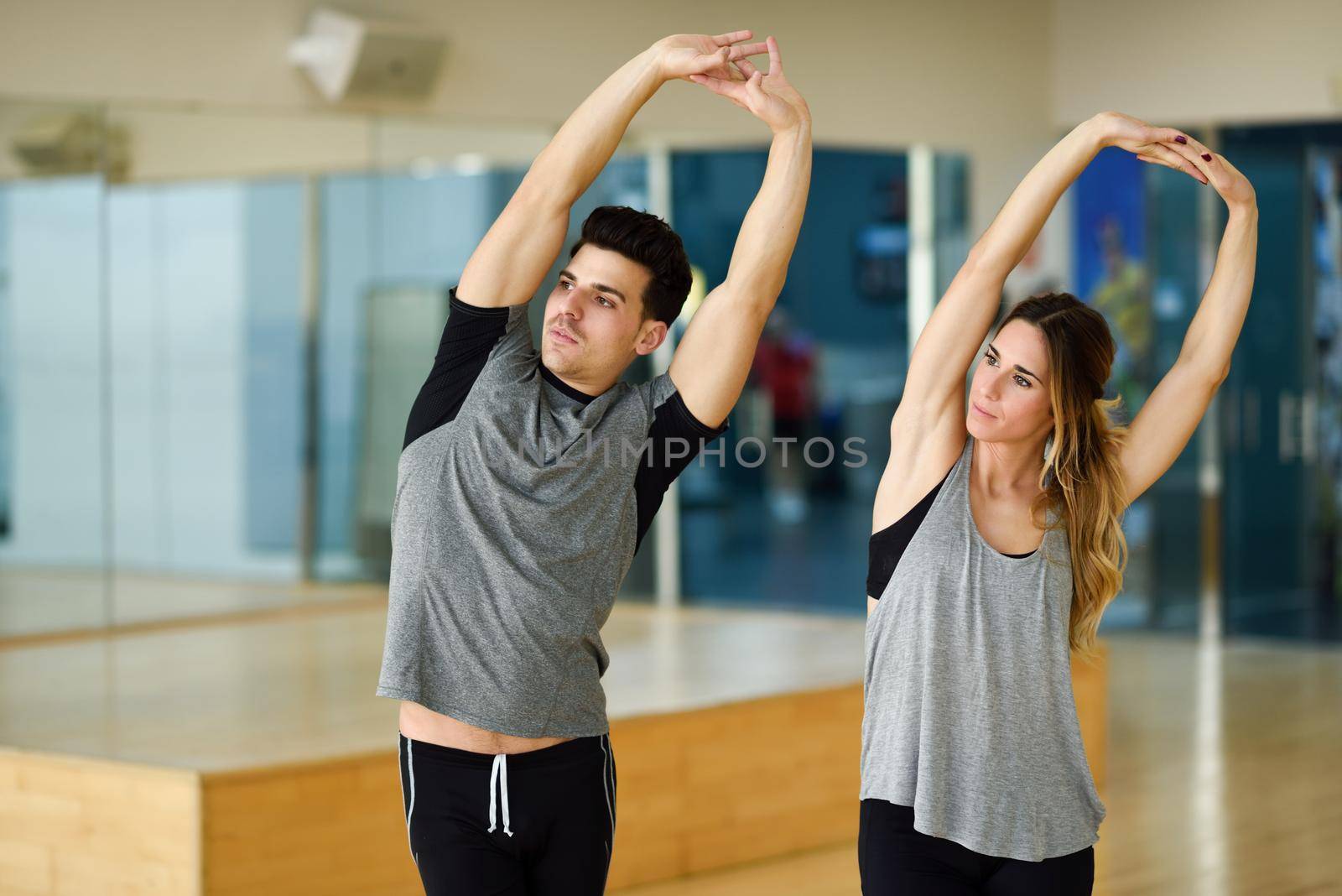 Young woman and man working out indoors. Two people stretching their arms in a gym.