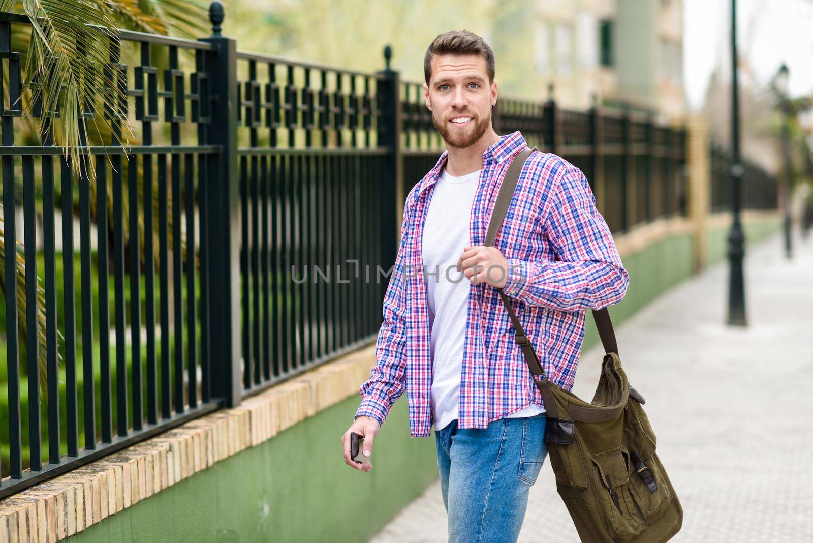 Young bearded man walking in urban background. Traveler wearing casual clothes. Lifestyle concept.