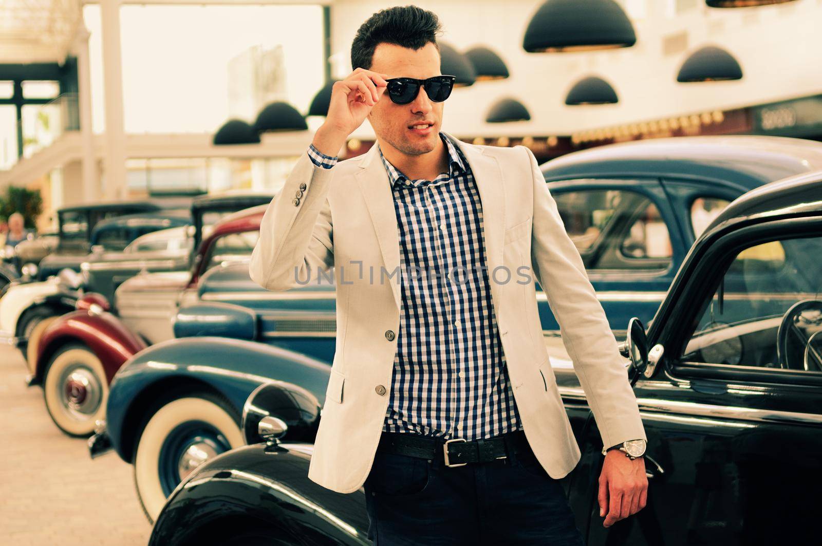 Portrait of a young handsome man, model of fashion, wearing jacket and shirt with old cars