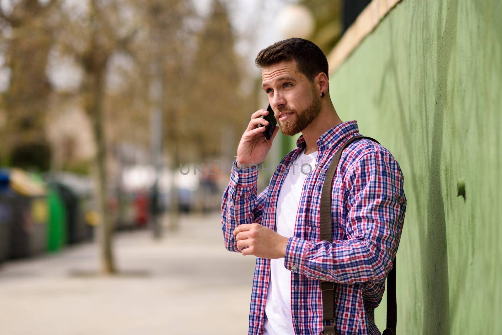 Young man talking with his smart phone in urban background. Guy wearing casual clothes. Lifestyle concept.
