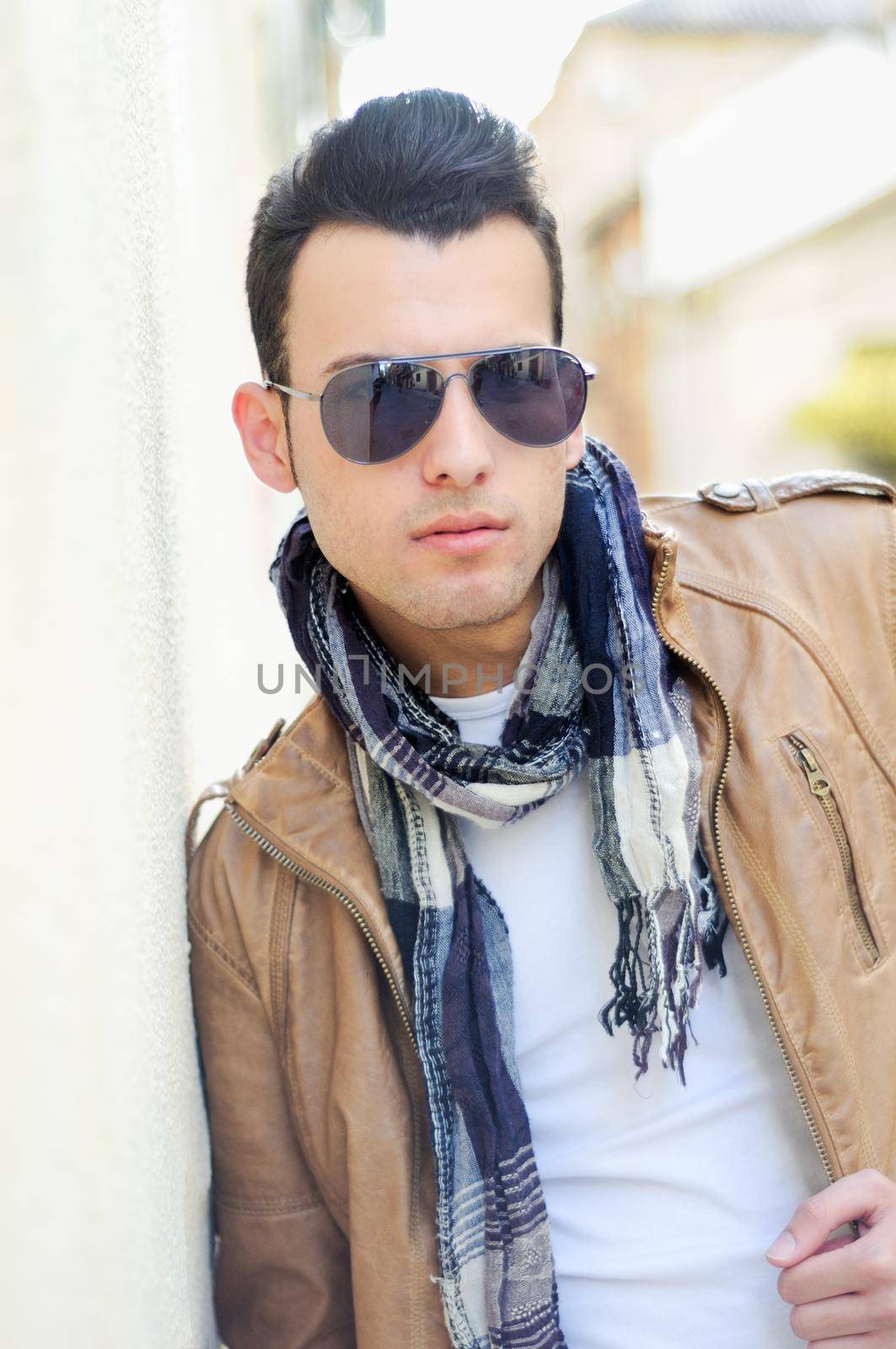 Portrait of a young handsome man, model of fashion, wearing tinted sunglasses in urban background