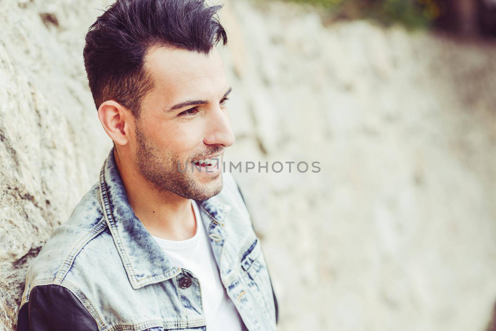 Portrait of a young handsome man, model of fashion, with modern hairstyle in urban background, smiling