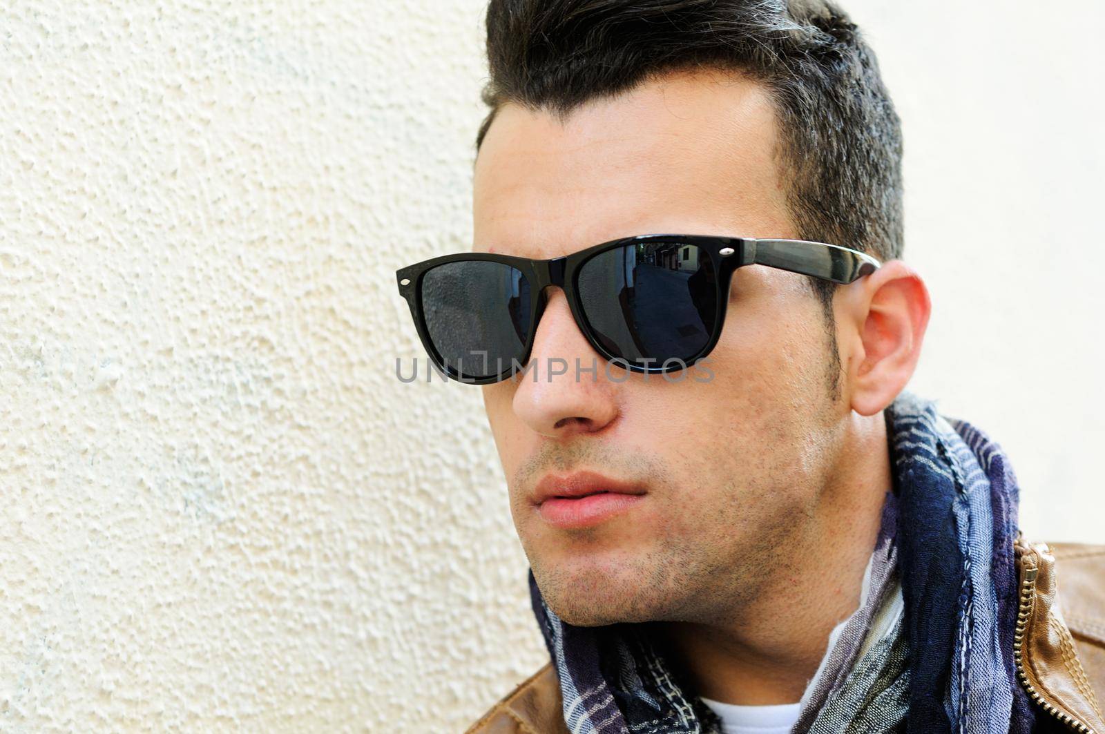 Portrait of a young handsome man, model of fashion, wearing tinted sunglasses in urban background