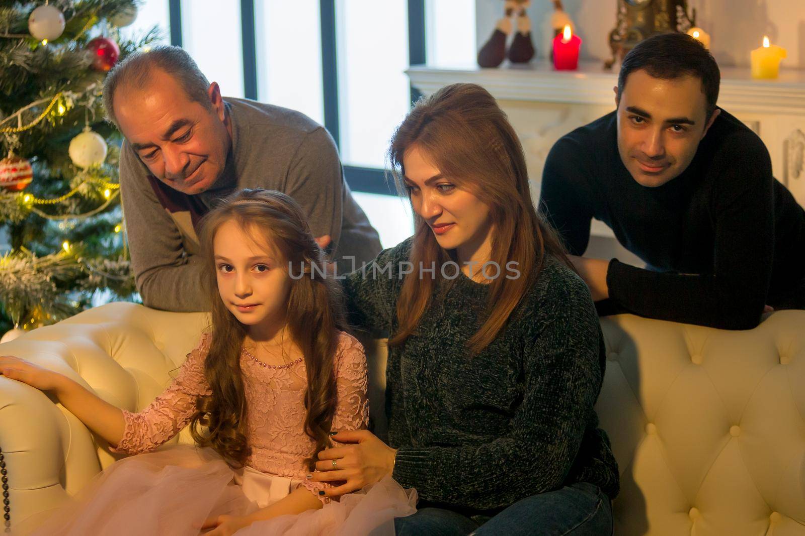 Parents hug their adorable daughter, mom and dad, as well as grandfather near the tree. by kolesnikov_studio