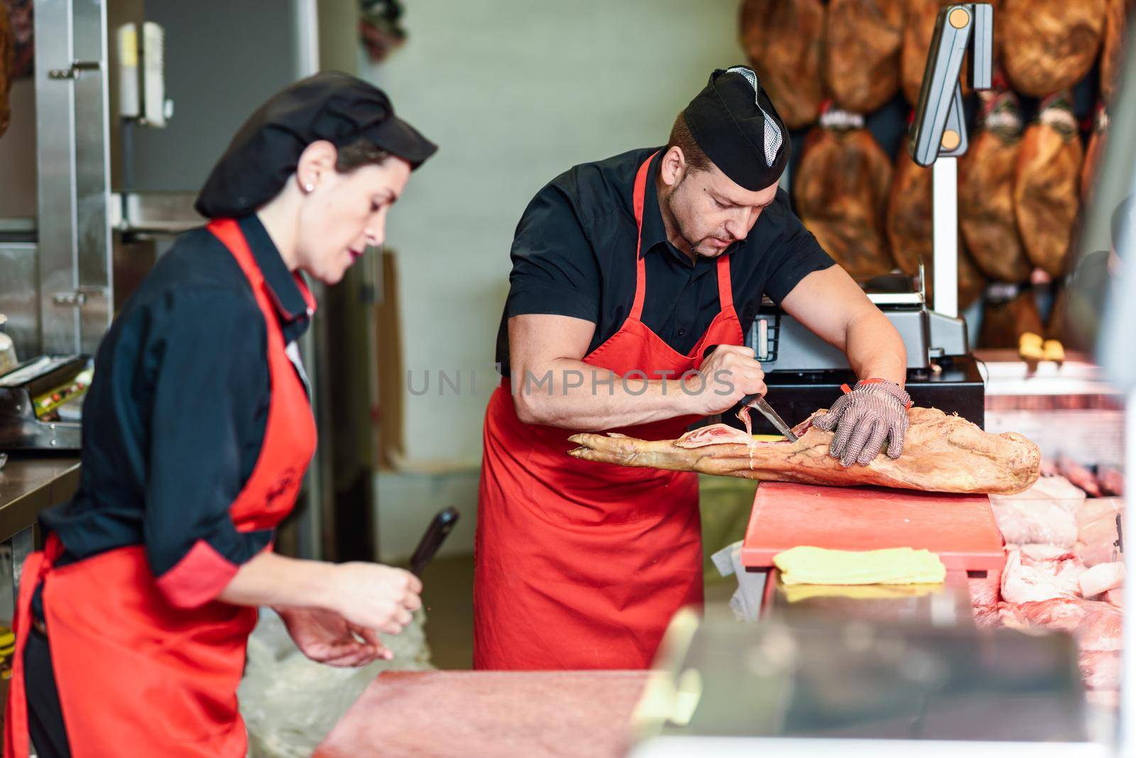 Male and female butchers boning a ham in a modern butcher shop