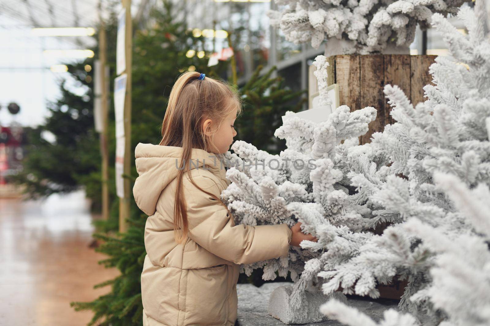 A girl and a white christmas artificial trees for sale on a shop