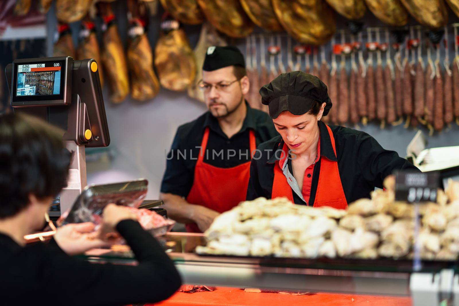 Butchers attending a customer in a butcher's shop weighing the meat and charging