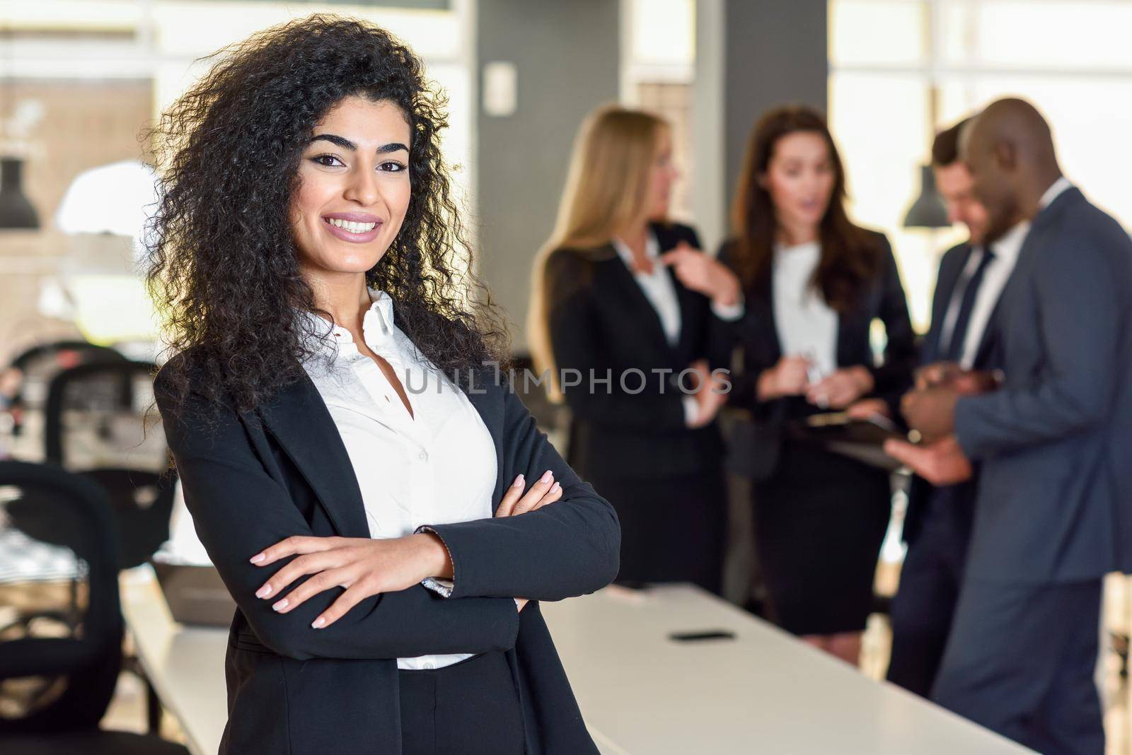 Businesswoman leader looking at camera in modern office with businesspeople working at the background. Teamwork concept. Muslim woman.