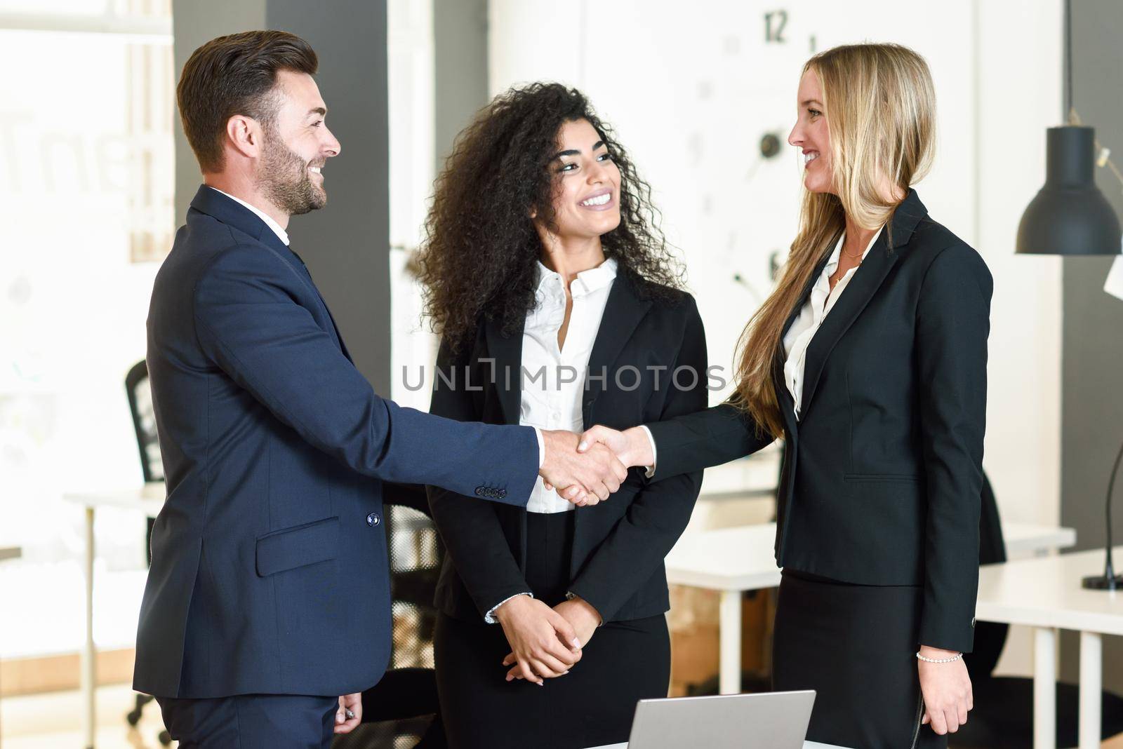 Multi-ethnic group of three businesspeople meeting in a modern office. Caucasian man and woman shaking hands wearing suit.