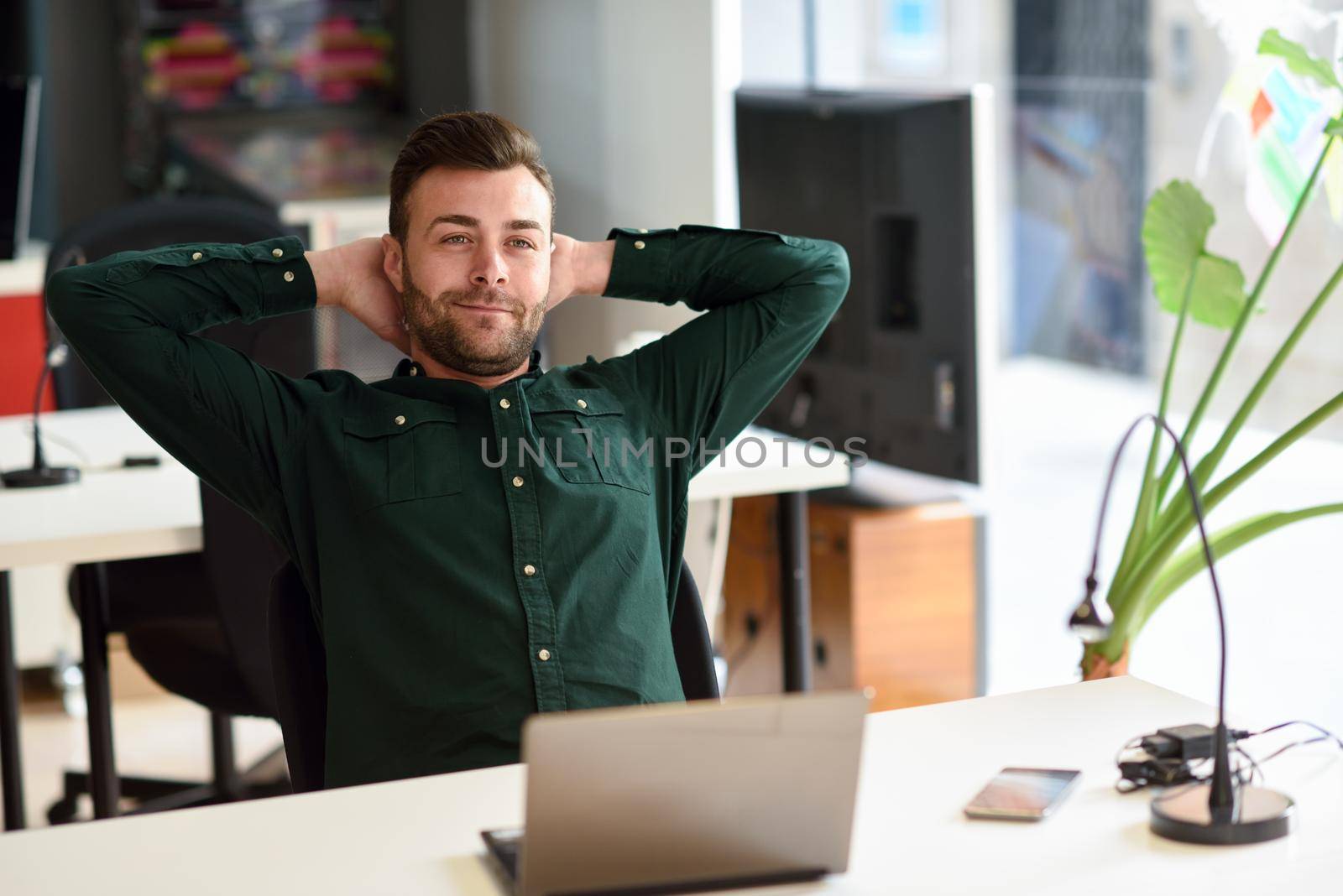 Young man studying with laptop computer on white desk. Attractive guy with beard wearing casual clothes taking a break.