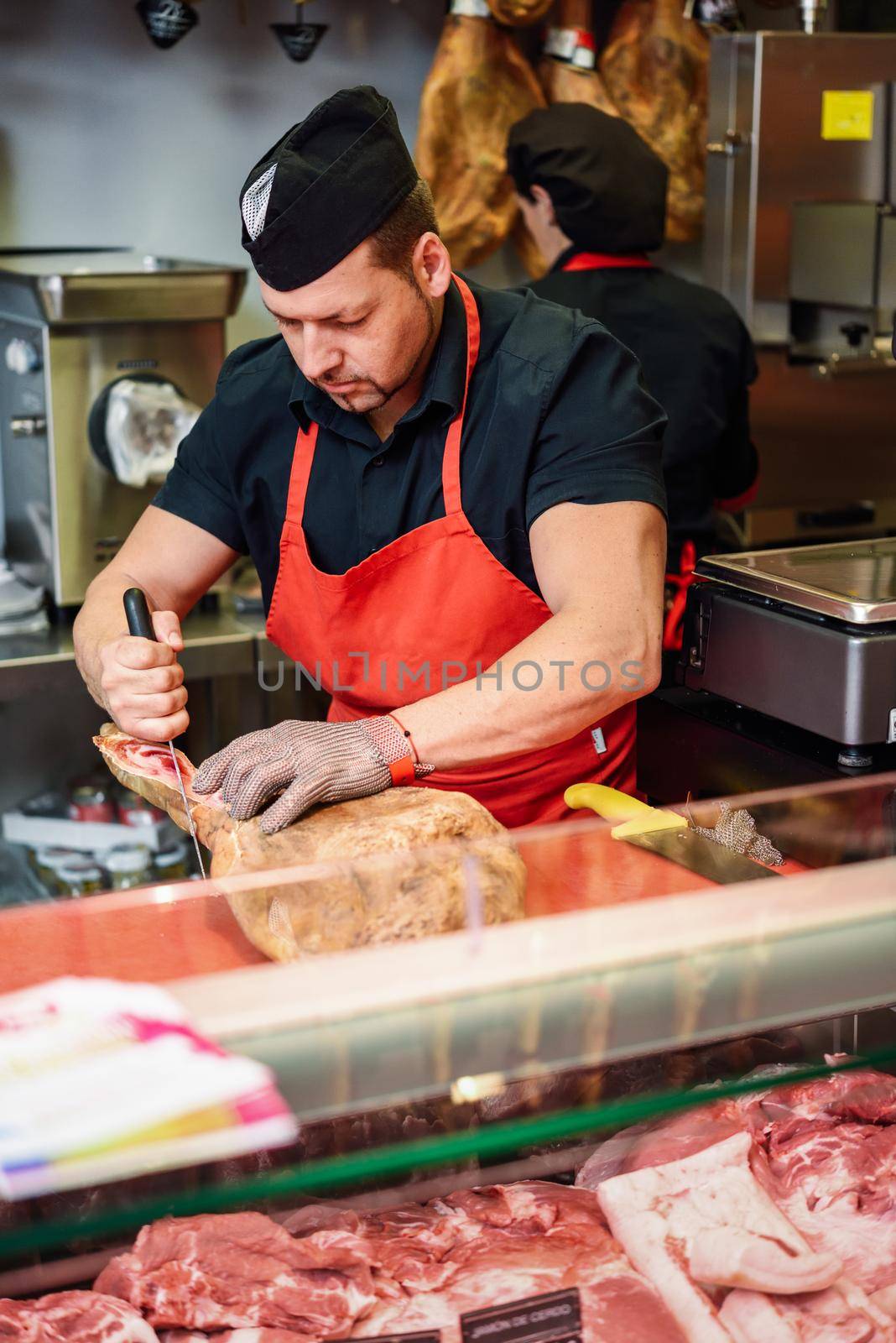 Male butcher boning a ham in a modern butcher shop with metal safety mesh glove