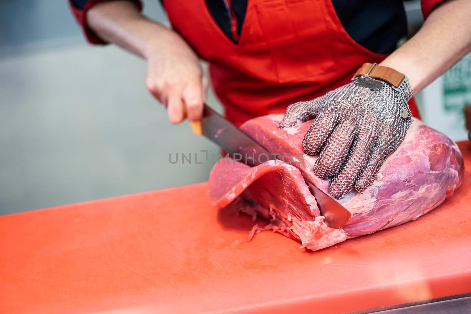 Female butcher cutting fresh meat in a butcher shop with metal safety mesh glove