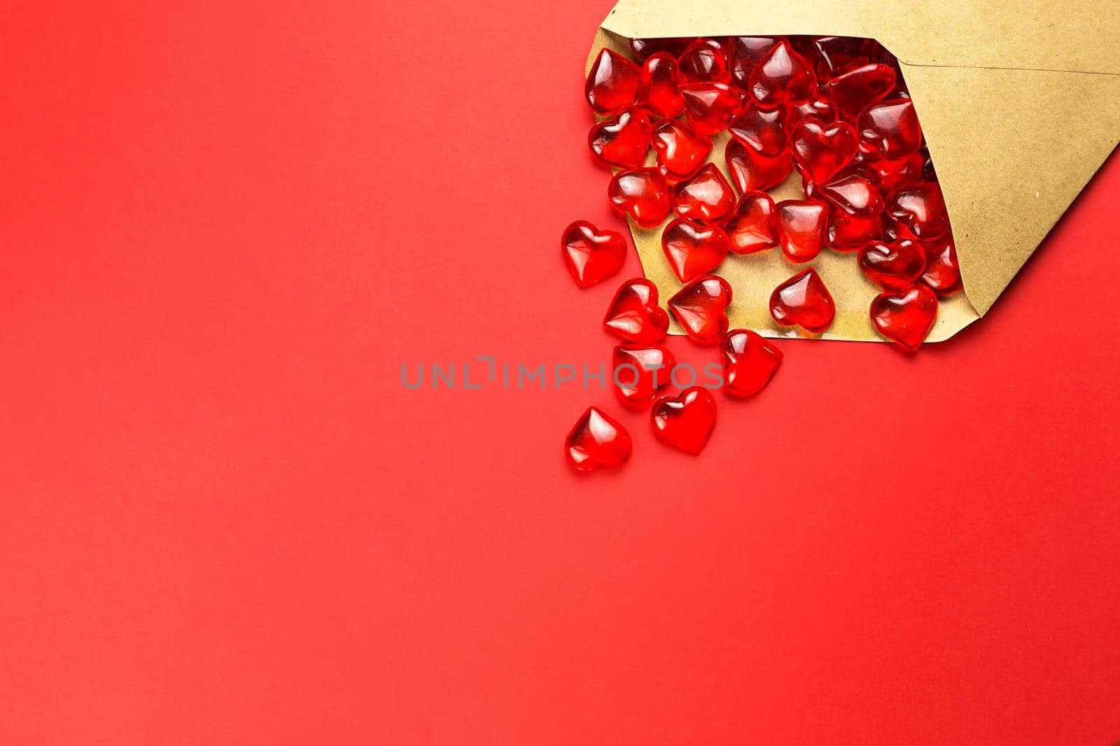 Glass hearts spill out of an open envelope on a red background. Valentine's Day, love letter, declaration of love, acquaintance. Copy space, mock up by Simol