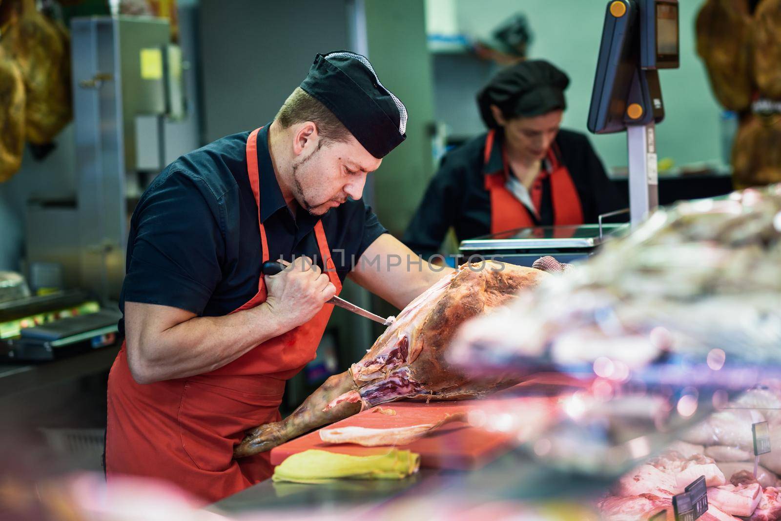 Male and female butchers boning a ham in a modern butcher shop