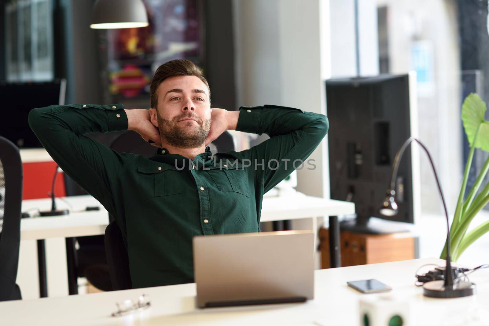 Young man studying with laptop computer on white desk. Attractive guy with beard wearing casual clothes taking a break.