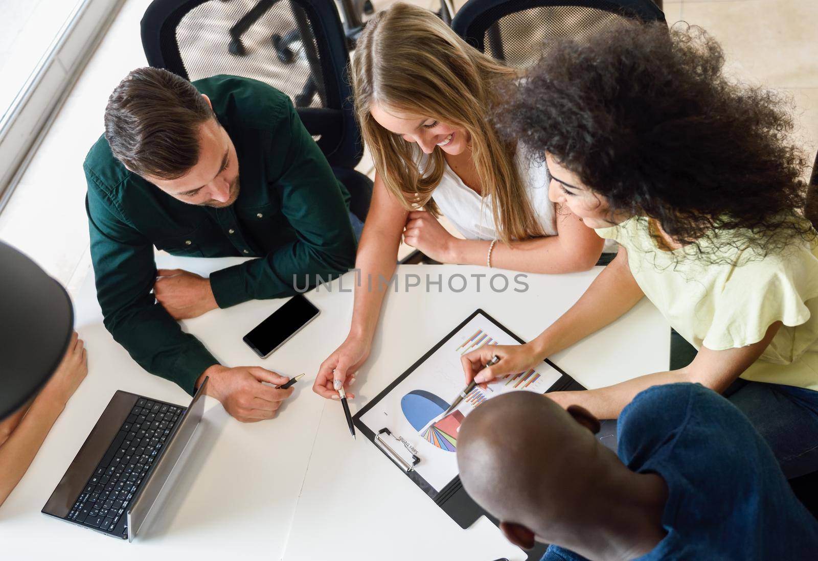Young people studying with laptop computer on white desk. Beautiful women and men working together wearing casual clothes. Multi-ethnic group. Top view