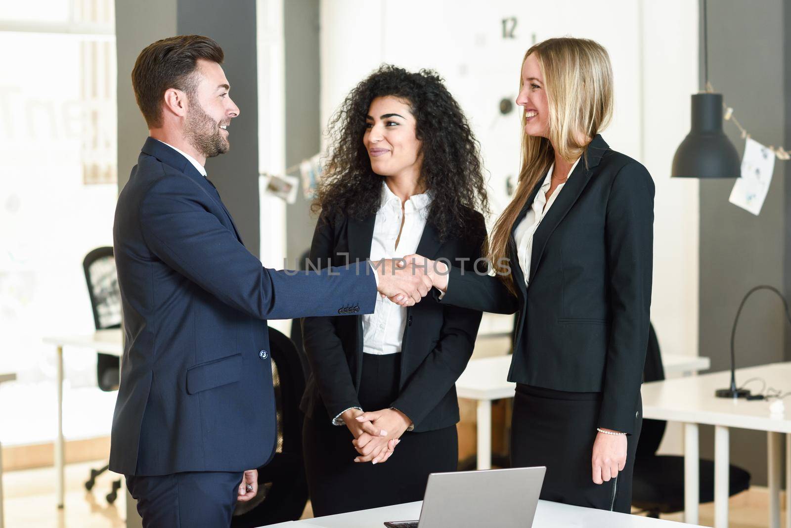Multi-ethnic group of three businesspeople meeting in a modern office. Caucasian man and woman shaking hands wearing suit.