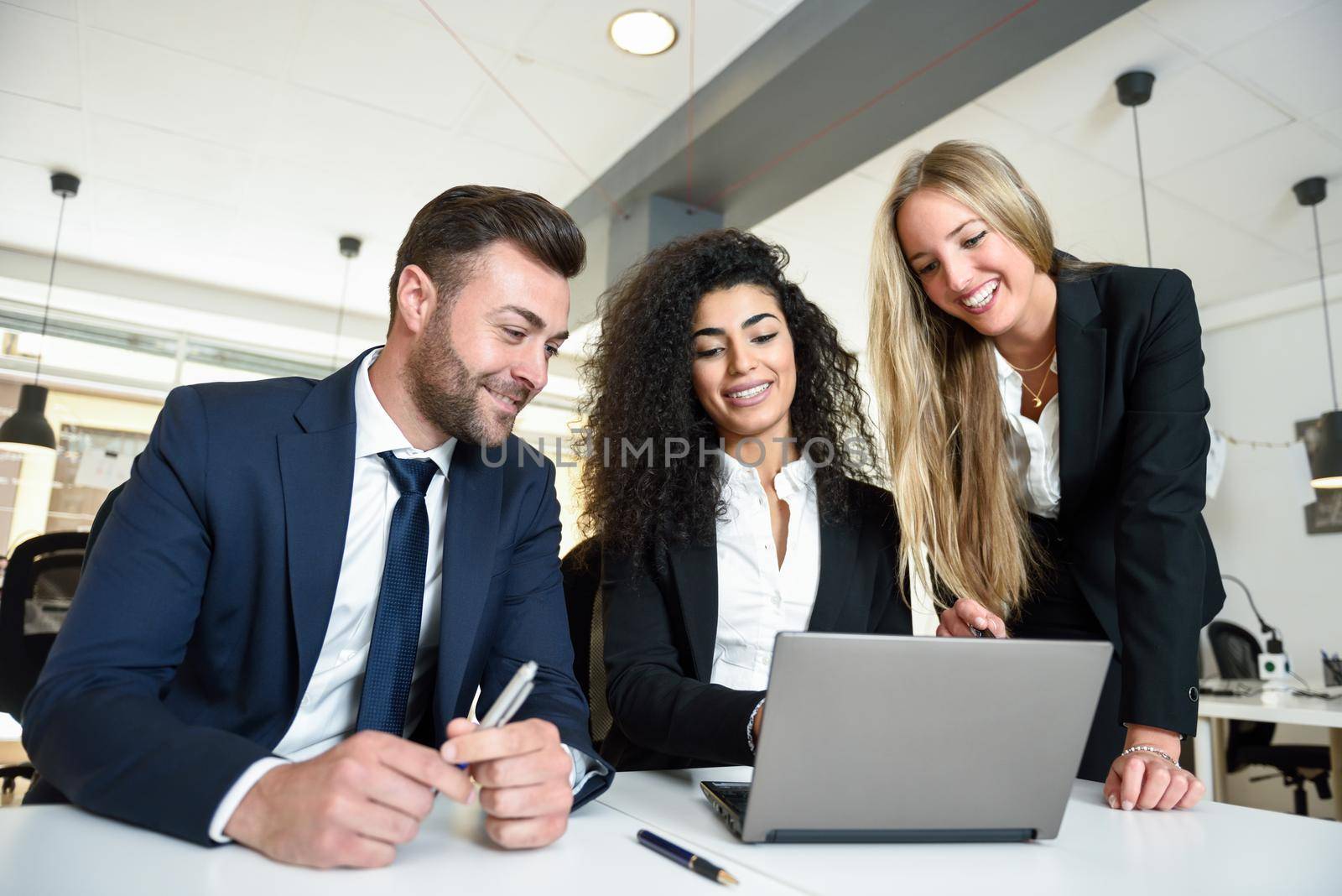 Multi-ethnic group of three businesspeople meeting in a modern office. Two women and a man wearing suit looking at a laptop computer.