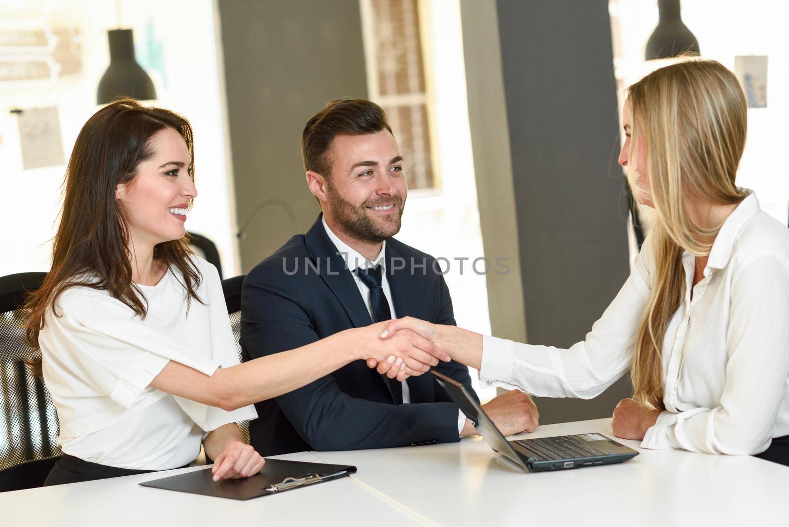 Smiling young couple shaking hands with an insurance agent or investment adviser. Three people meeting in an office reaching an agreement