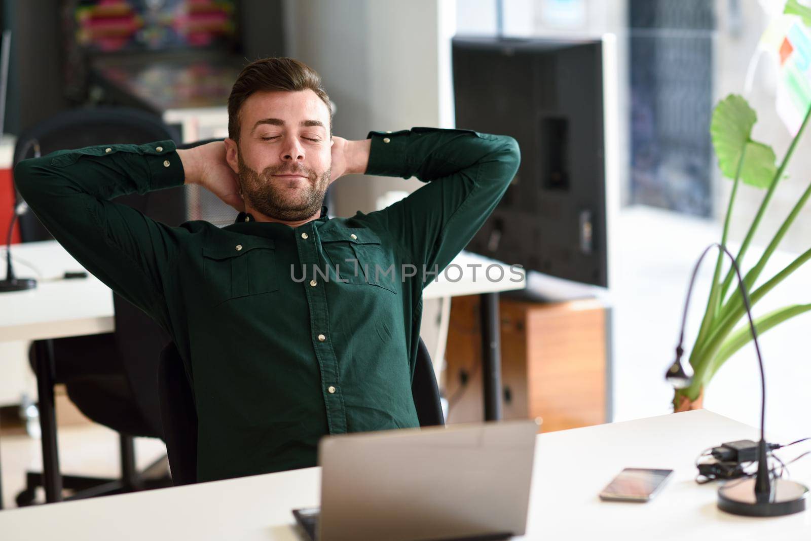 Young man studying with laptop computer on white desk. Attractive guy with beard wearing casual clothes taking a break.