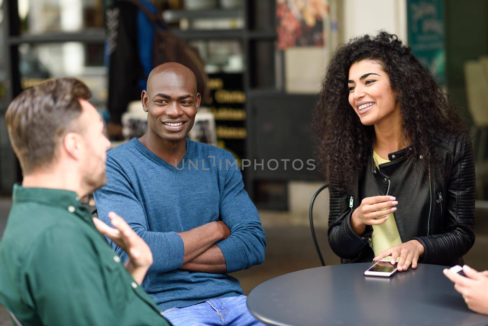 Multiracial group of friends waiting for a coffee together. Two men and a man sitting at cafe, talking and smiling. Lifestyle and friendship concepts with real people models