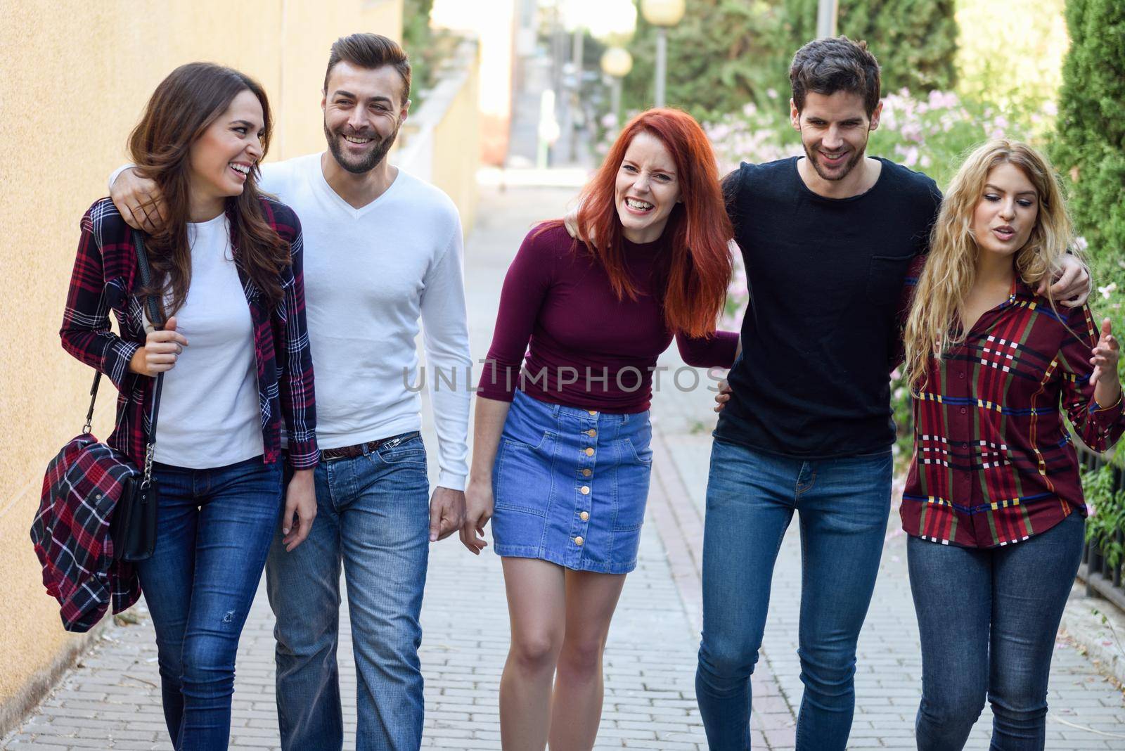 Group of young people together outdoors in urban background. Women and men sitting on stairs in the street wearing casual clothes.