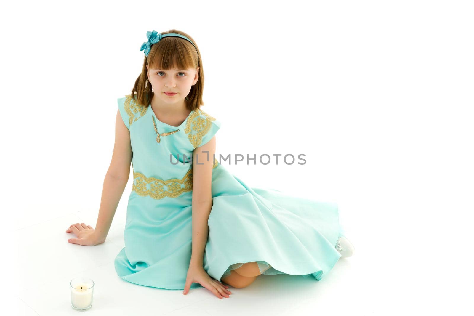 Beautiful little girl kneels in the studio on a white background. The concept of beauty and fashion, children's emotions. Isolated on a white background.