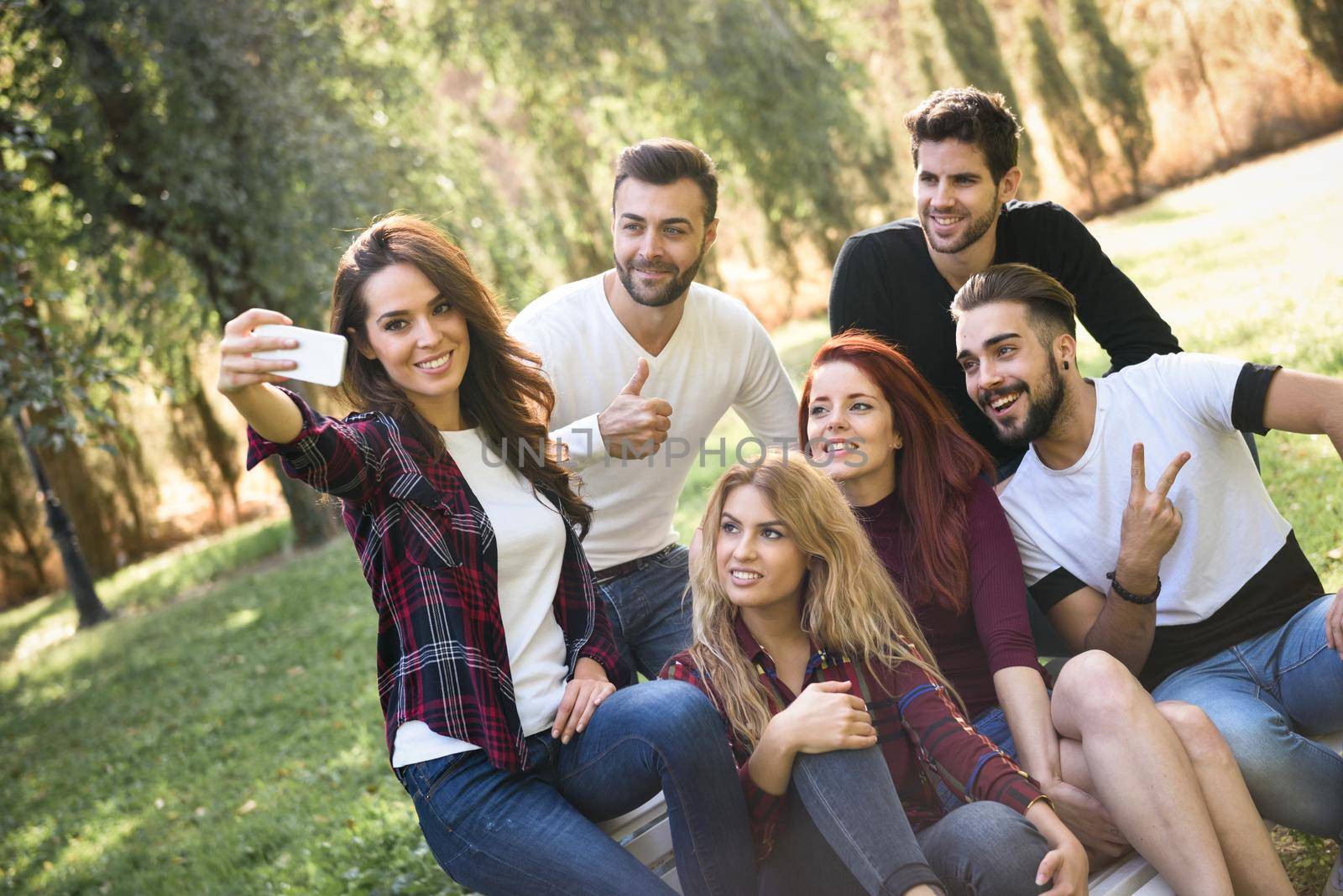 Group of friends taking selfie in urban park. Five young people wearing casual clothes.