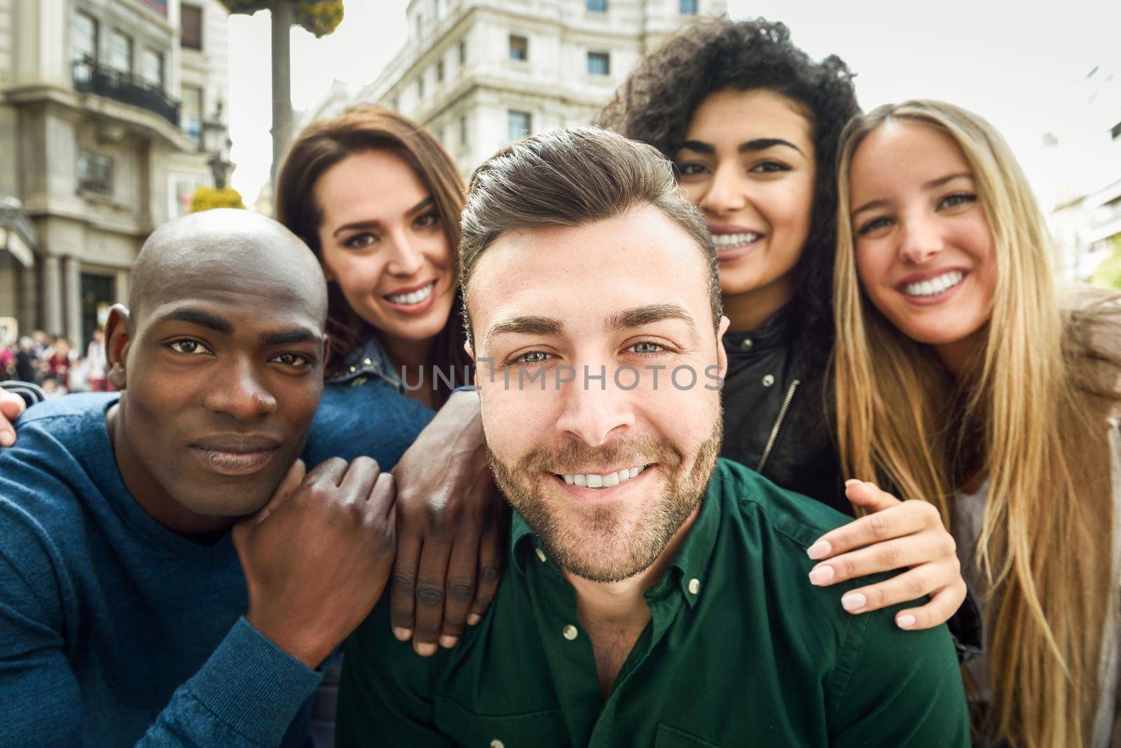 Multiracial group of friends taking selfie in a urban street with a caucasian man in foreground. Three young women and two men wearing casual clothes.