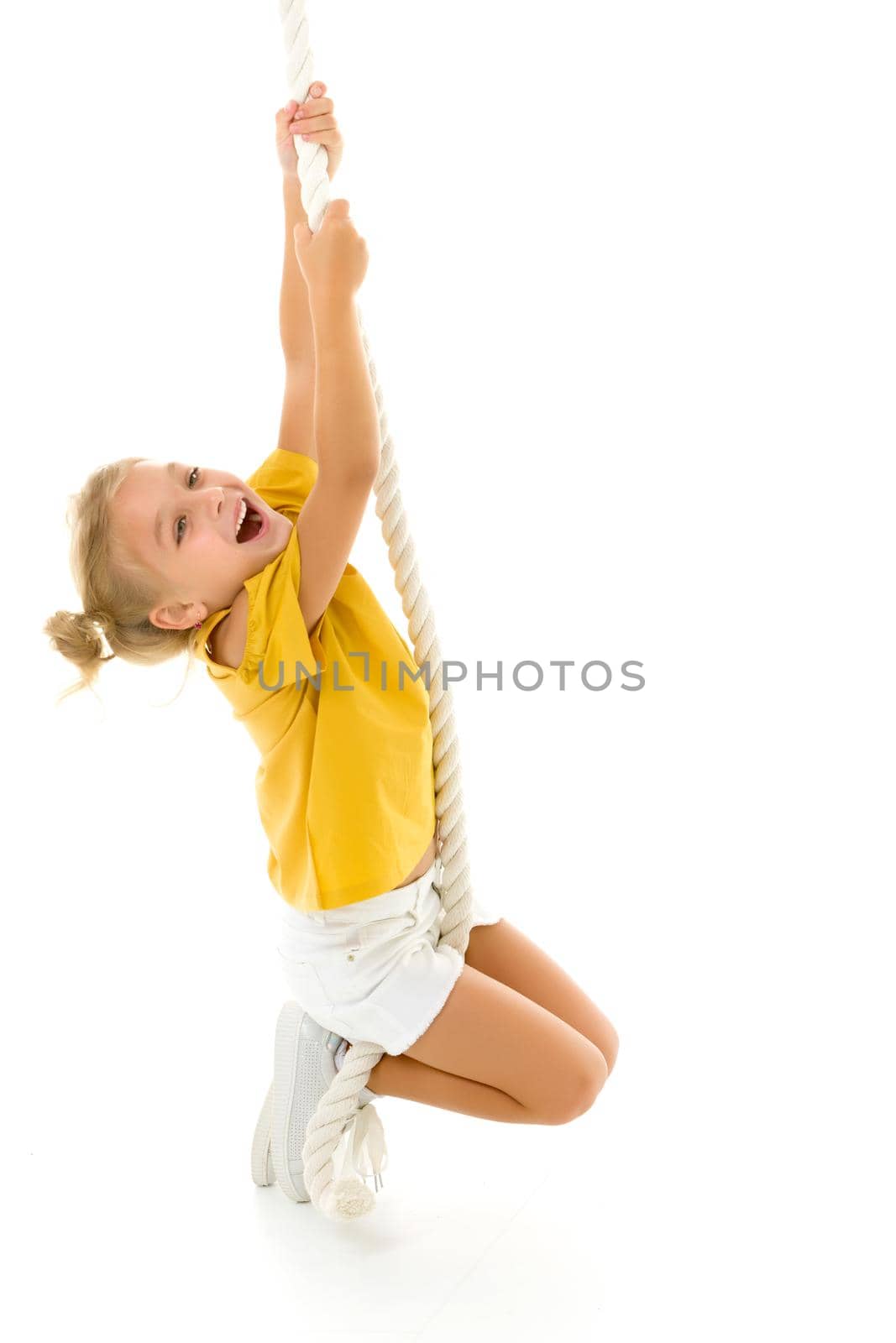 Cheerful little girl holding a rope with her hands. She tries to swing from side to side on it. Sport, fitness concept. Isolated over white background.