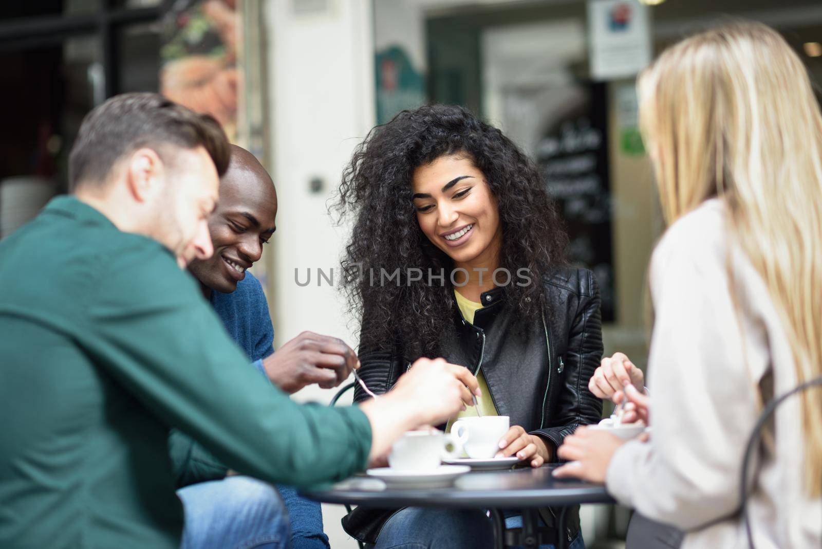 Multiracial group of four friends having a coffee together. Two women and and two men at cafe, talking, laughing and enjoying their time.