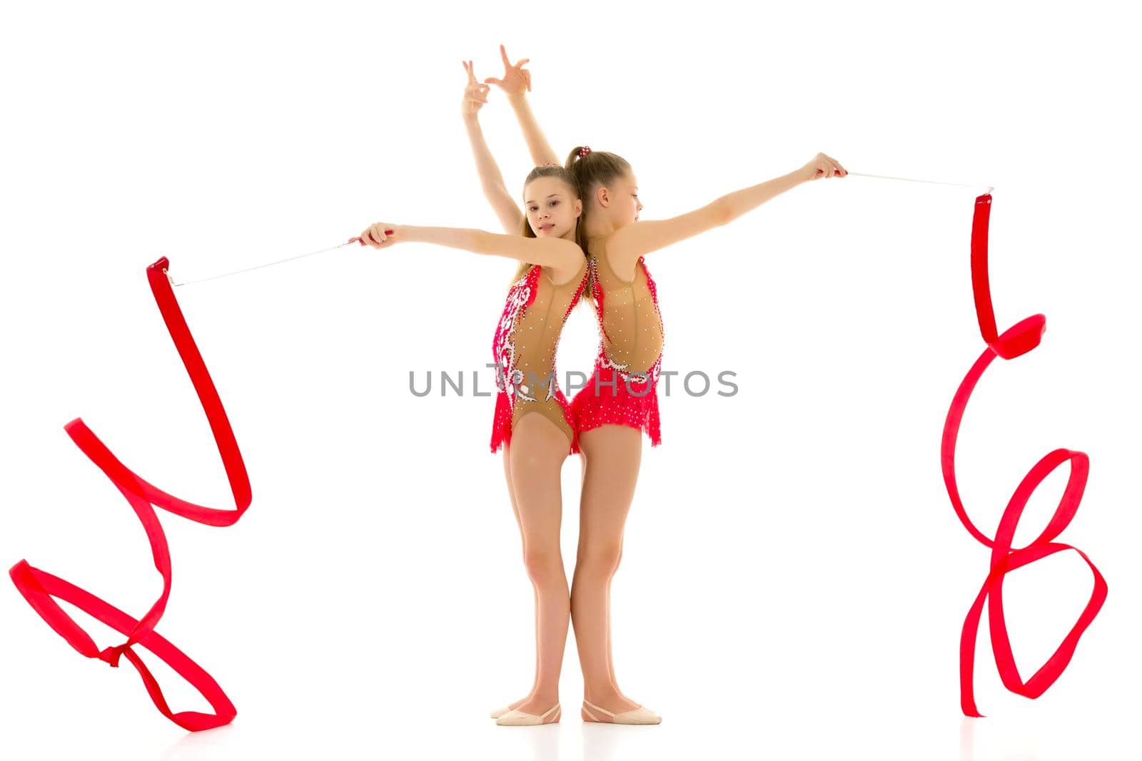 Two charming girls gymnasts, beautiful costumes for the competition, perform synchronized movements with a ribbon. The concept of children's sport, fitness. Isolated on a white background.