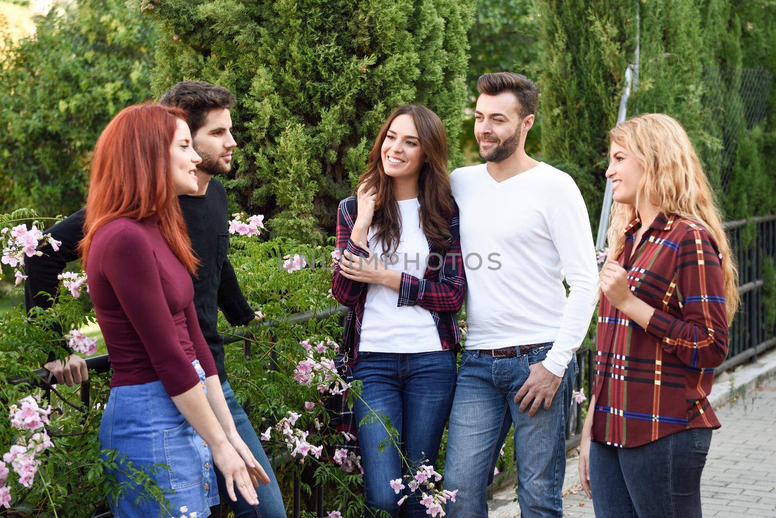 Group of young people together outdoors in urban background. Women and men sitting on stairs in the street wearing casual clothes.