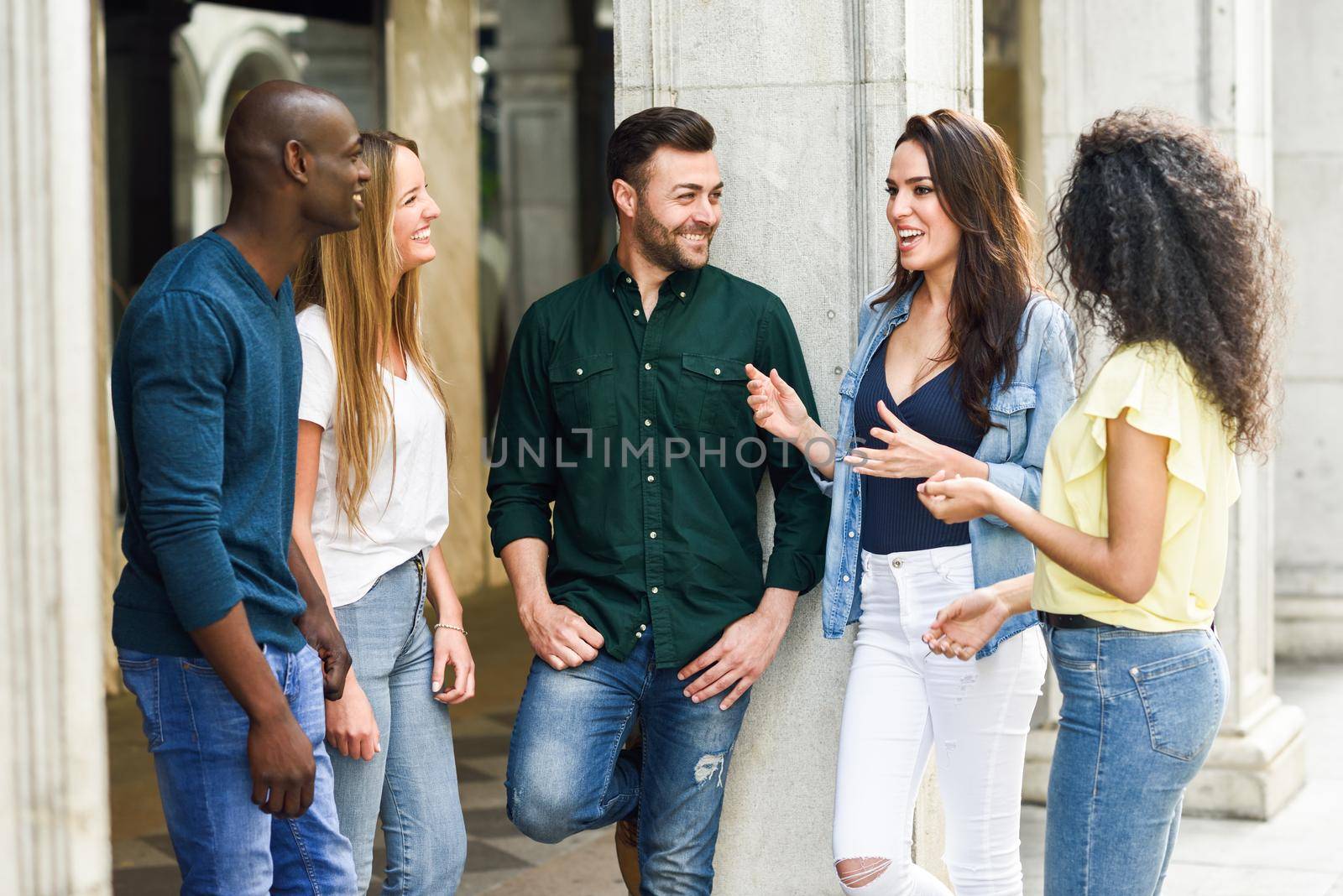 Multi-ethnic group of young people having fun together outdoors in urban background. group of beautiful women and men laughing together