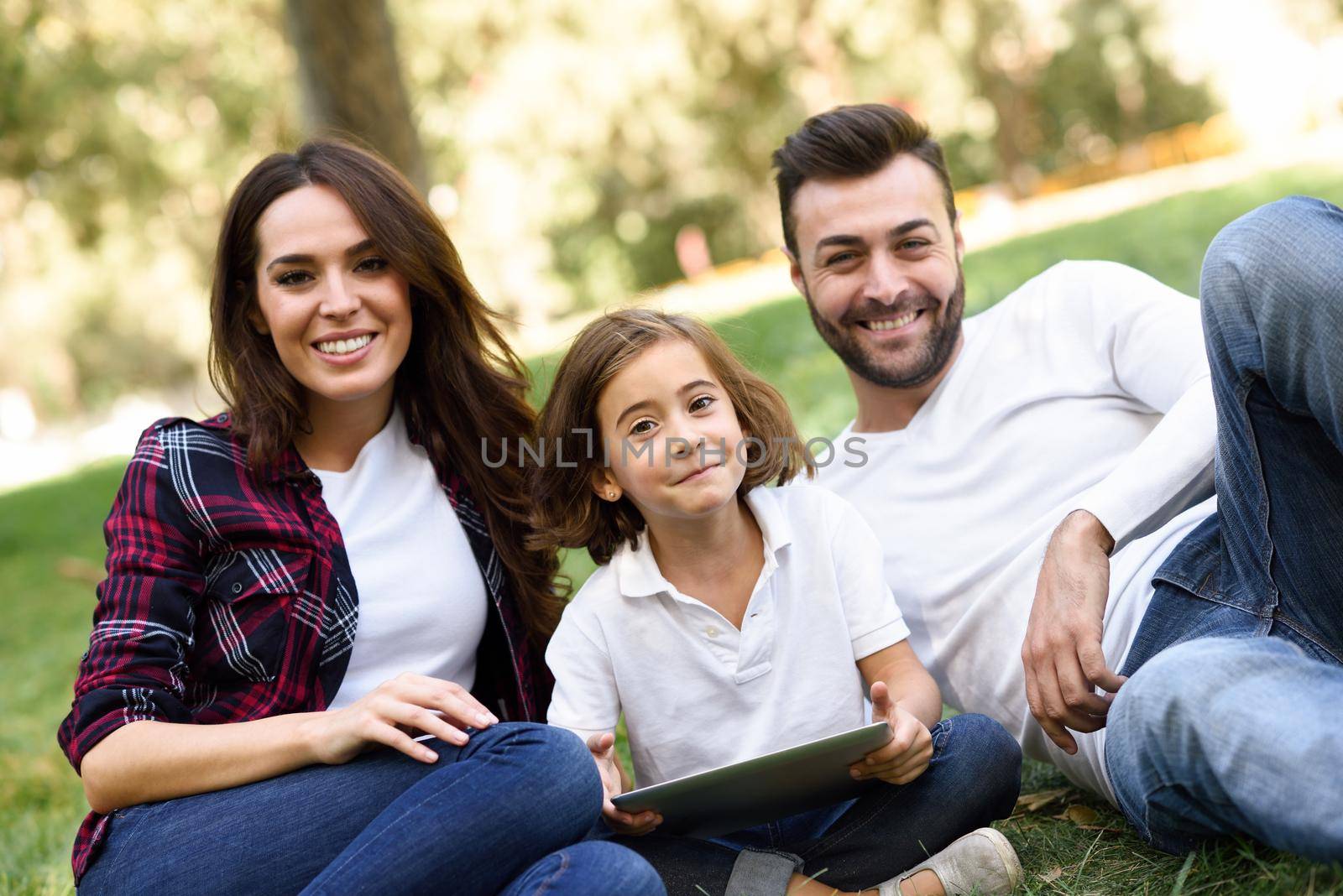 Happy family in a urban park playing with tablet computer by javiindy